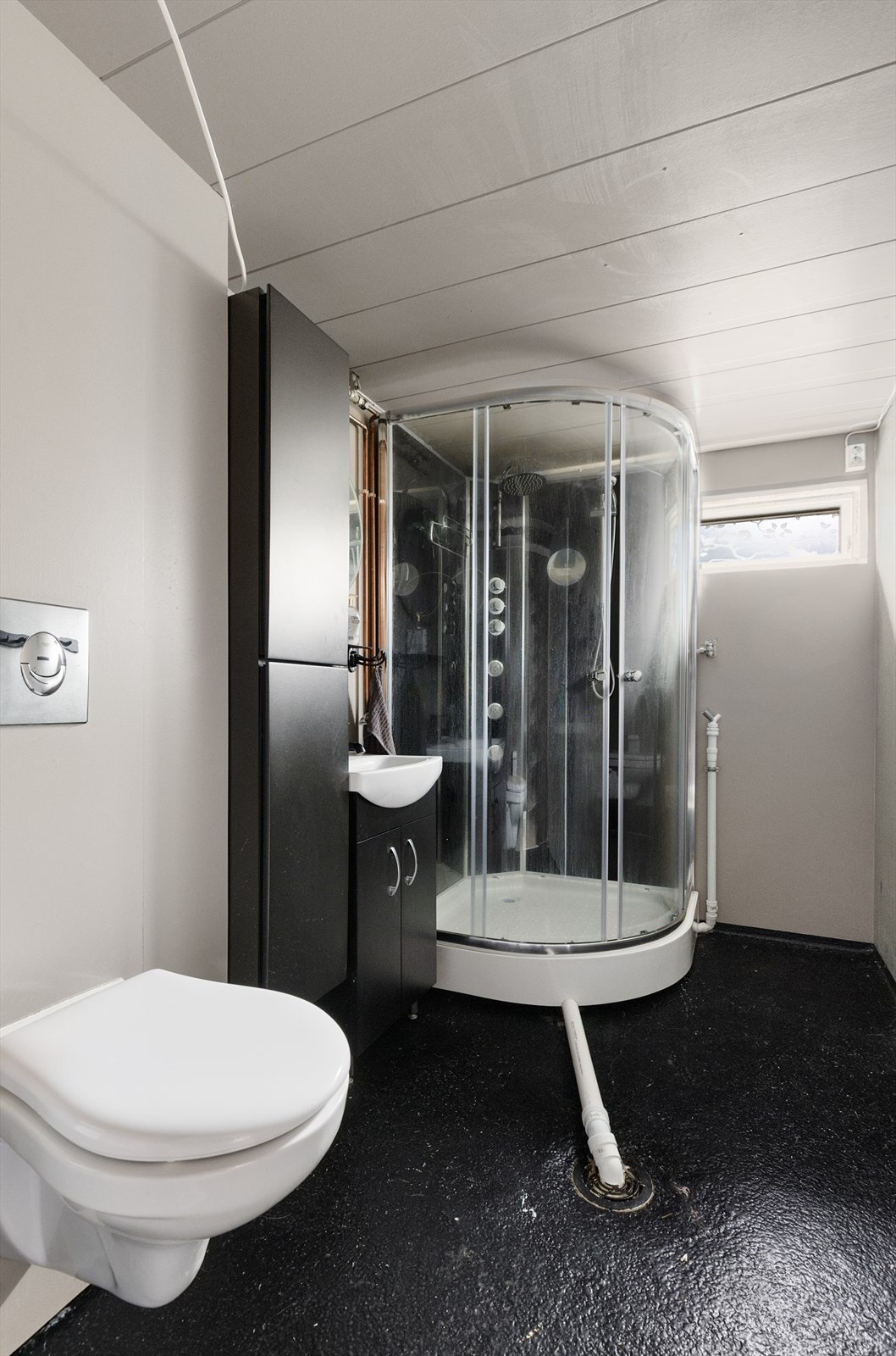 Bad fra byggeår med malt betonggulv og malte plater på vegger. Her er det vegghengt toalett, dusjkabinett og innredning med heldekkende vask, underskap og høyskap. Rommet har også opplegg for vaskemaskin.
Innredning og utstyr er av nyere dato. Galleribilde