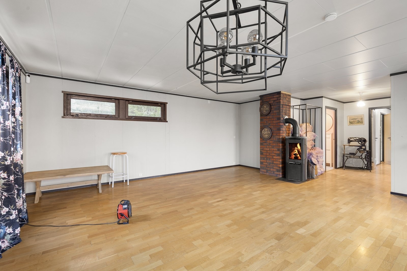 Her er det parkett på gulv og malte plater på vegger. Sentralt i rommet er det plassert en vedovn. Galleribilde