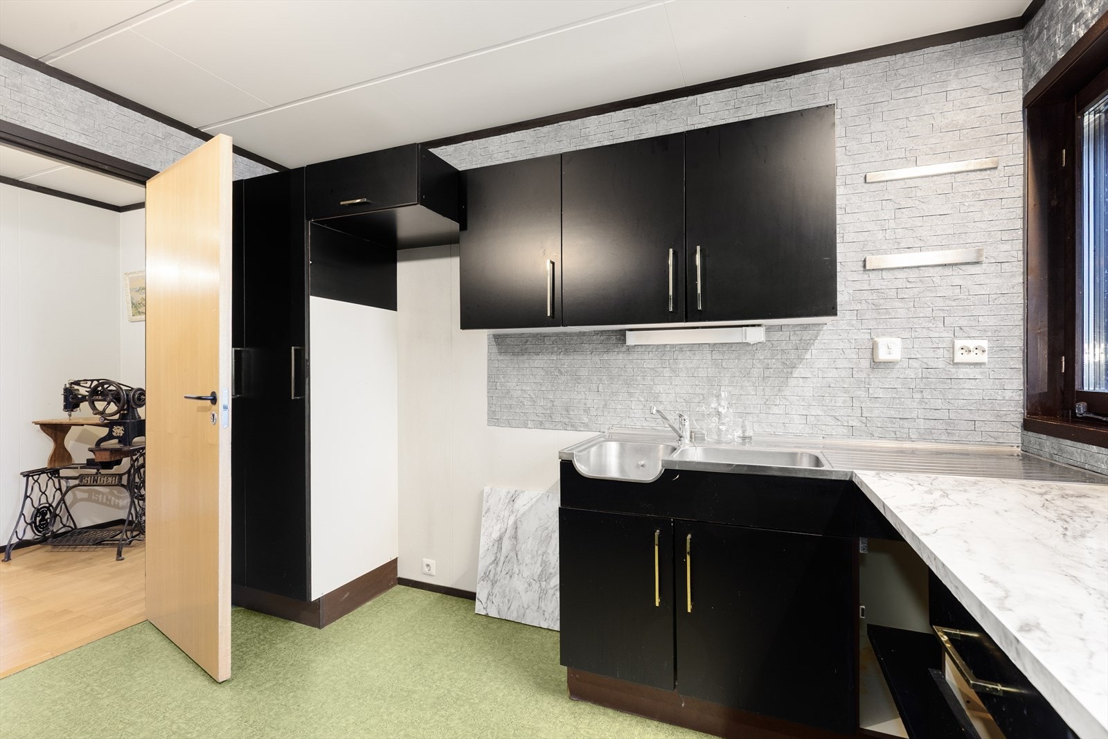 Kjøkkenet har en eldre innredning med slette fronter, laminat benkeplate og benkebeslag. Det er ventilator med avtrekk ut, montert i skap over komfyr. Galleribilde