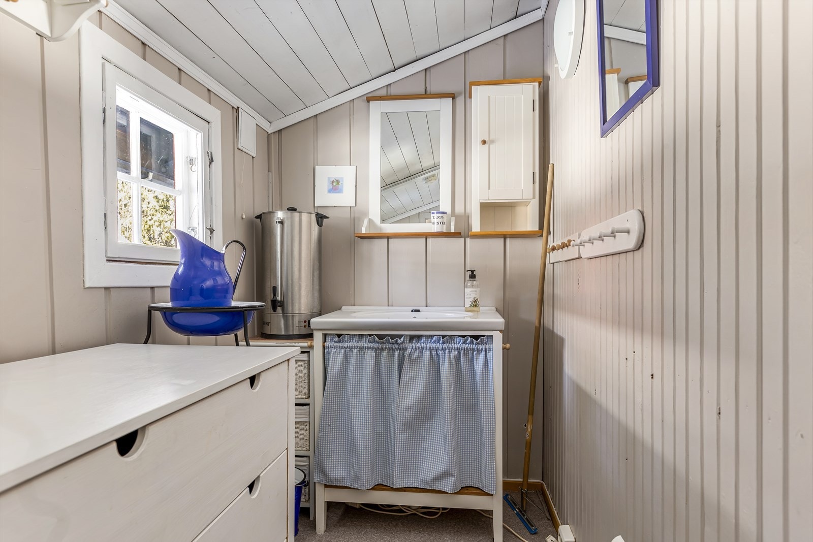 På vaskerommet er det enkelt servantskap med forheng og porselensservant med avløp til terreng. Det er oppbevaringsplass i kommoder, og det en vannvarmer gir enkel tilgang på varmt vann. Galleribilde