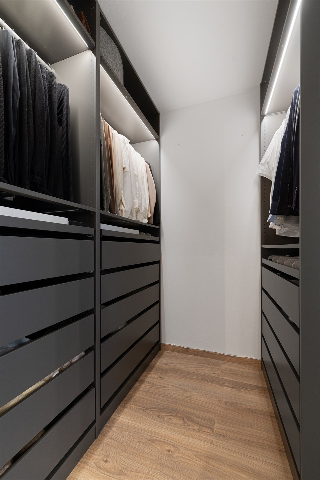 Omkledningsrommet har garderobeløsninger på begge sider og integrert belysning. Rikelig med plass til oppbevaring av klær, sko og tilbehør Galleribilde