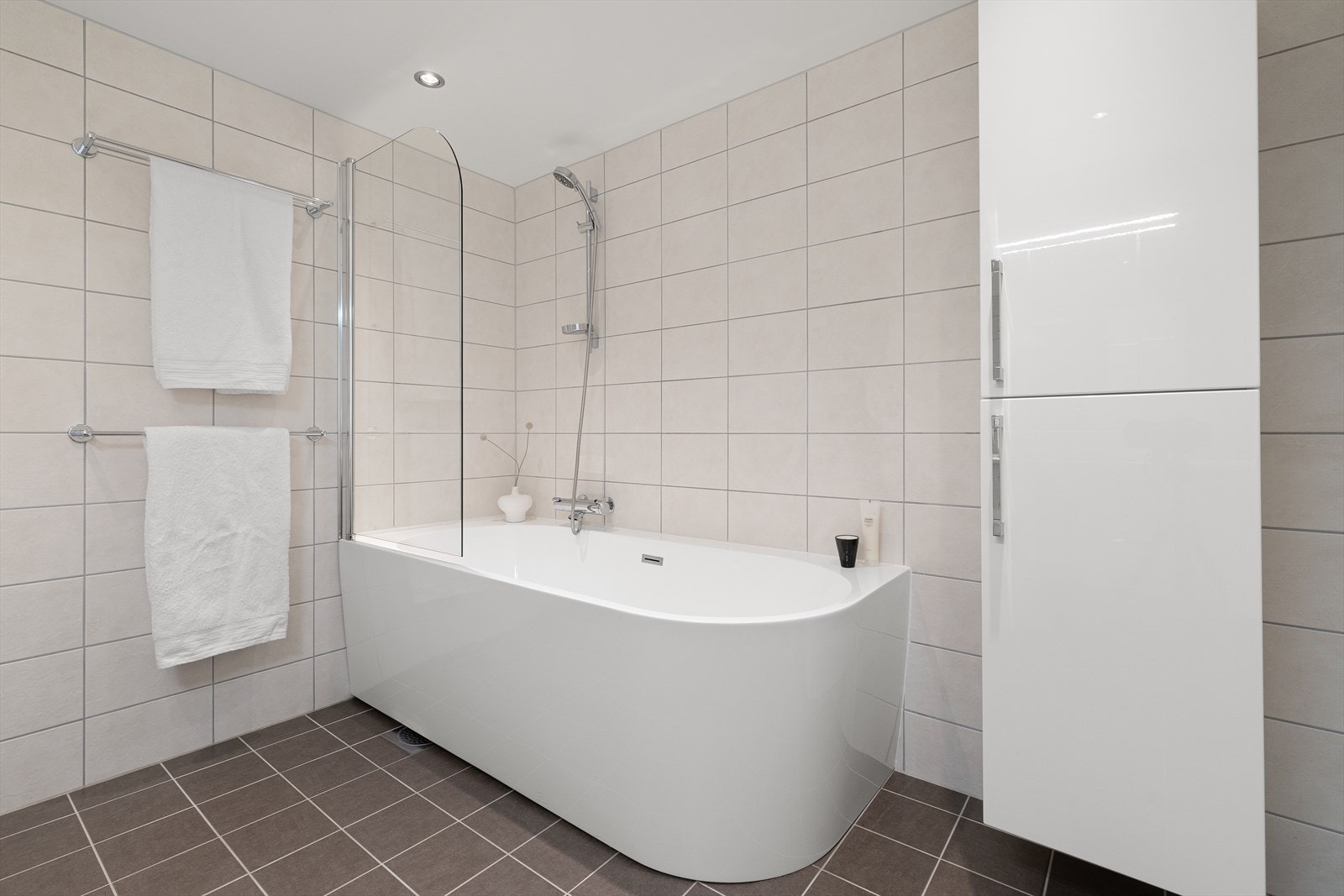 Badet er innredet med vegghengt toalett, høyskap samt badekar med dusjvegg i glass Galleribilde