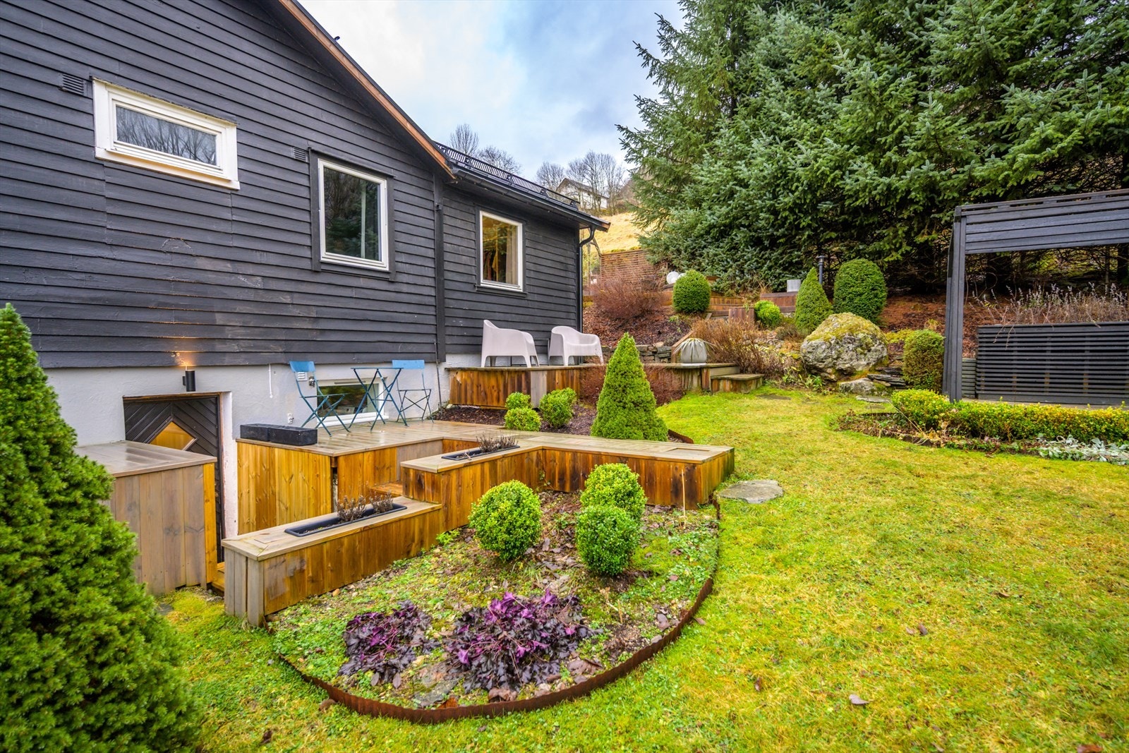Huset er omrammet av plen og blomsterbed. Det er anlagt steinmurer. Trapper og blomsterkasser er i impregnert trevirke. Galleribilde