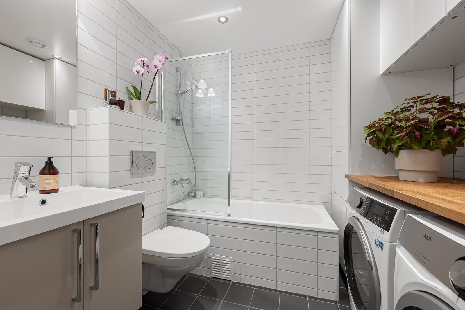 Praktisk bad kombinert med vaskerom, med badekar, benkeplass, oppbevaringsplass og opplegg for vaskemaskin og tørketrommel. Galleribilde