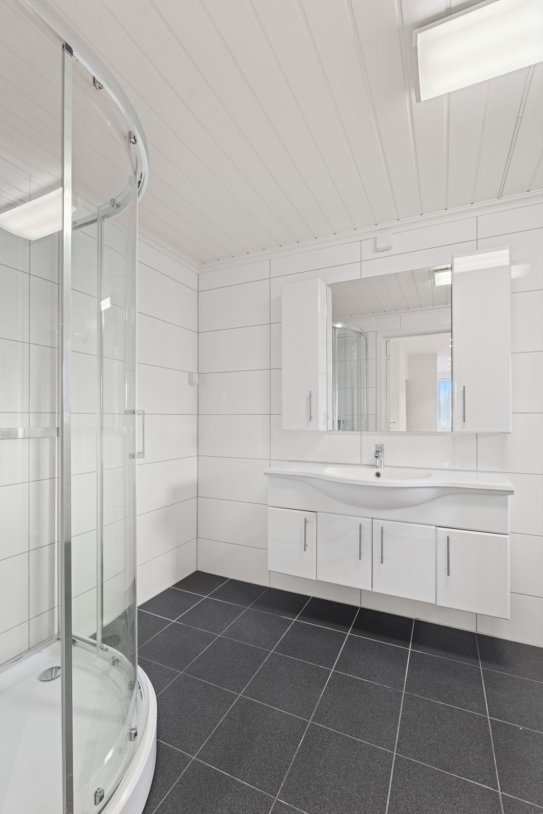 Baderom utstyrt med vaskeservant i innredning, gulvmontert wc og lukket dusjkabinett. Galleribilde