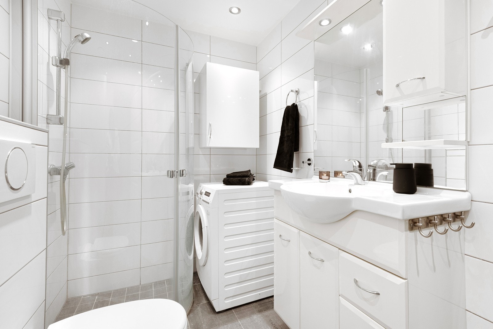 Badet har lyse flislagte overflater, downlights, gulvvarme og en tidløs innredning. For klesvask er det plass til vaskemaskin og vegghengte overskap for oppbevaring. Galleribilde