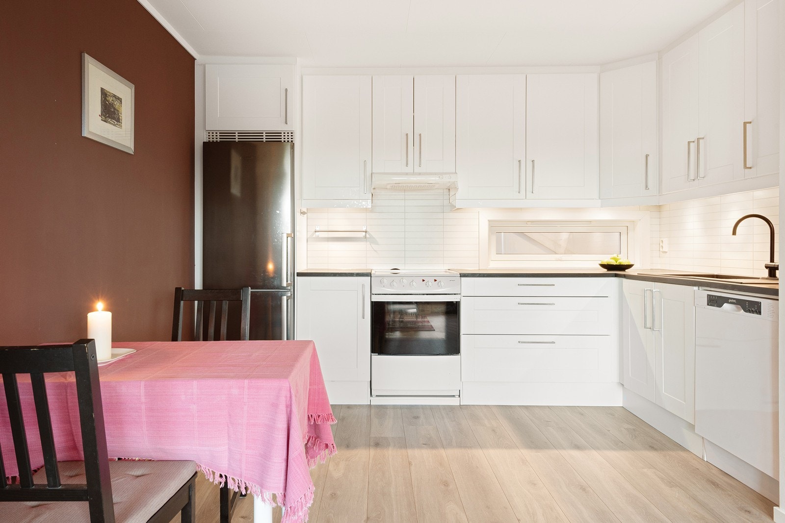 Kjøkkenet fremstår moderne og er praktisk plassert i en vinkel. Innredningen har hvite fronter og laminert benkeplate med nedfelt oppvaskkum i kompositt. Galleribilde