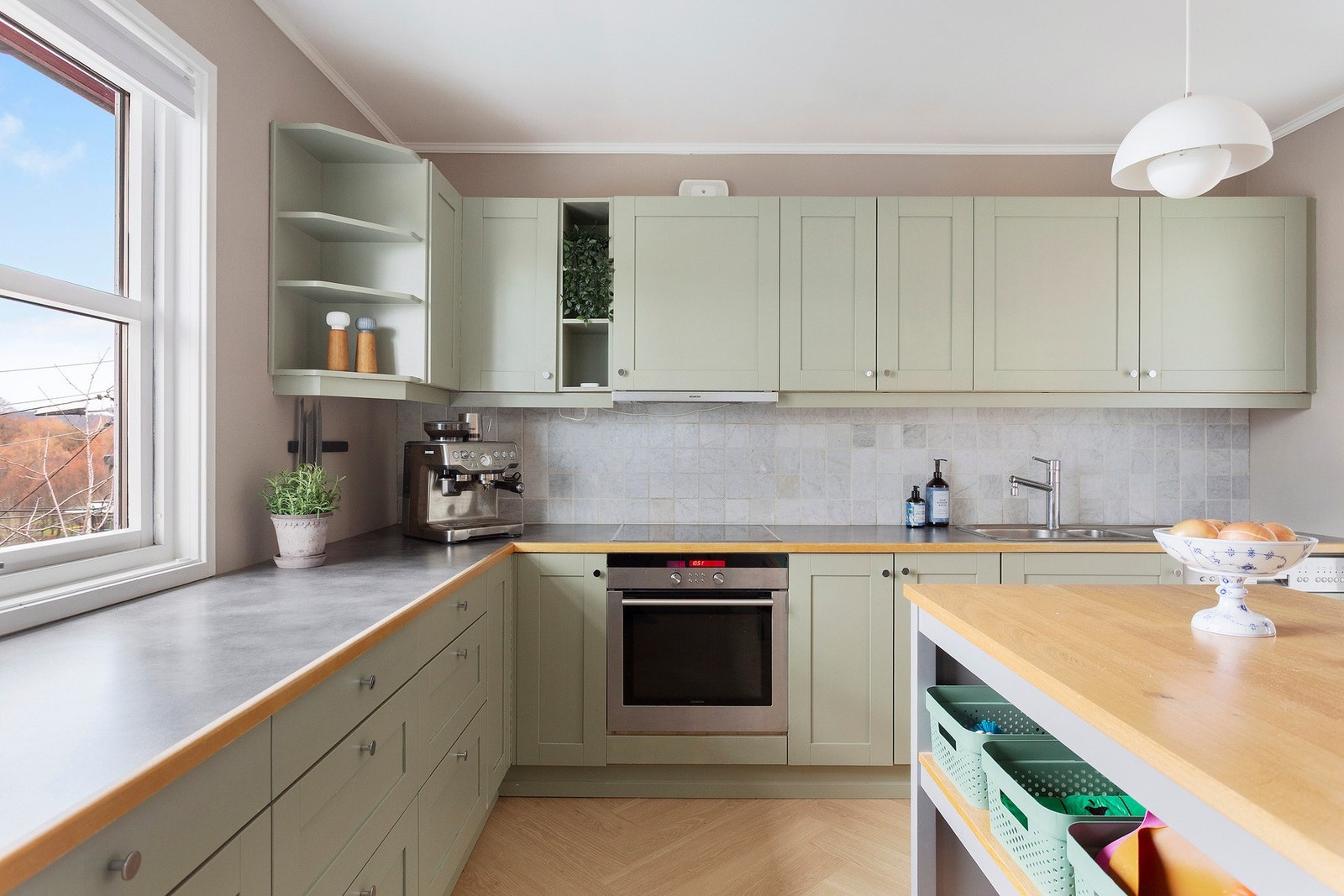 Lyst og innbydende kjøkken med delikate farger, rikelig oppbevaringsplass og en praktisk kjøkkenøy som skaper en fin sosial sone. Galleribilde