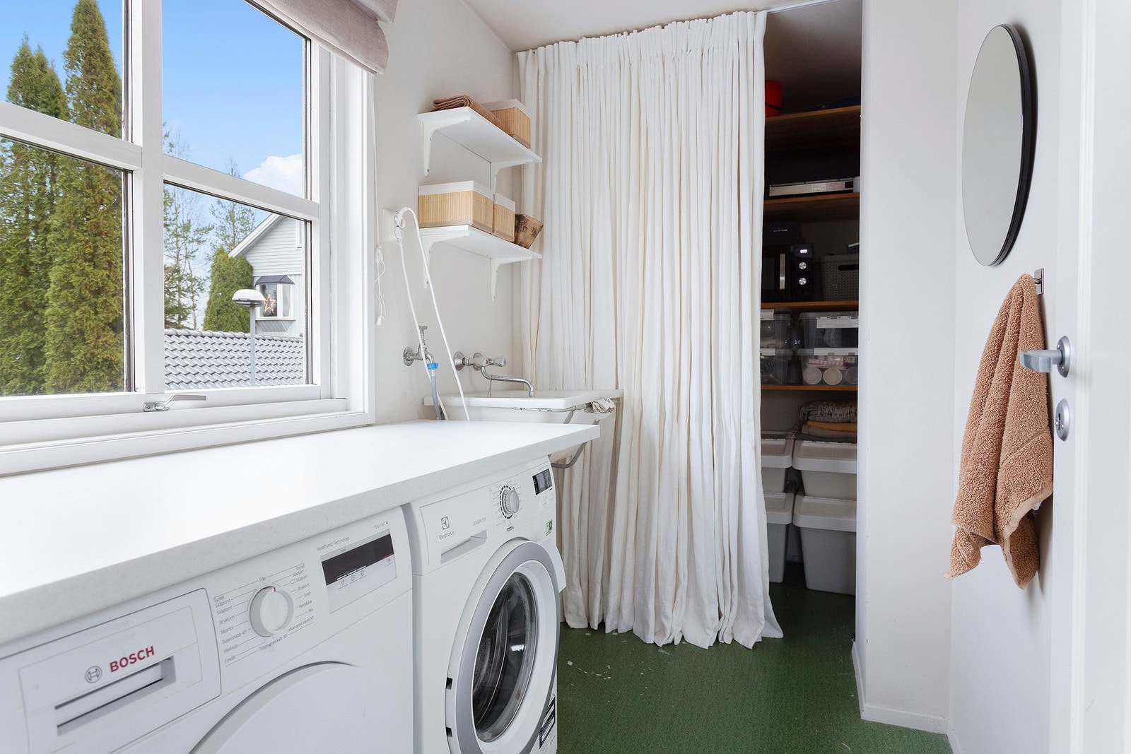Lyst og praktisk vaskerom med god benkeplass, arbeidskum og smart oppbevaring bak forheng. Galleribilde