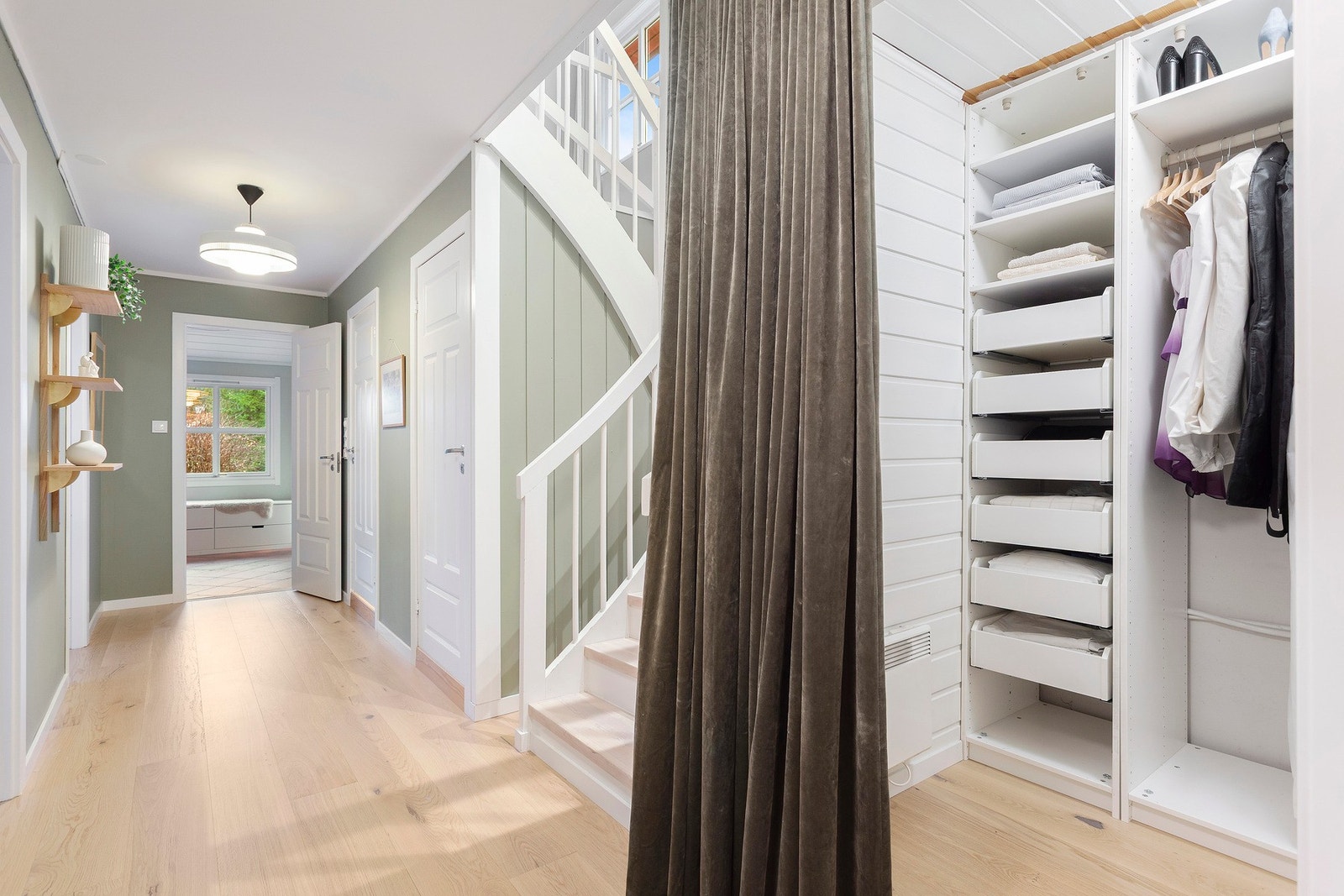 Lys og gjennomført gang med god plass til oppbevaring, lune materialvalg og en elegant trappeløsning som binder etasjene fint sammen. Galleribilde