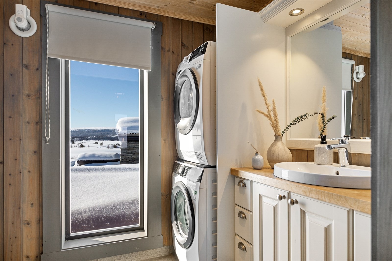 Hyttas bad er lyst og delikat med et høyt vindu som slipper lyset og naturen inn. Her er det pen baderomsinnredning i malt heltre med over og underskap, speil og belysning. Galleribilde