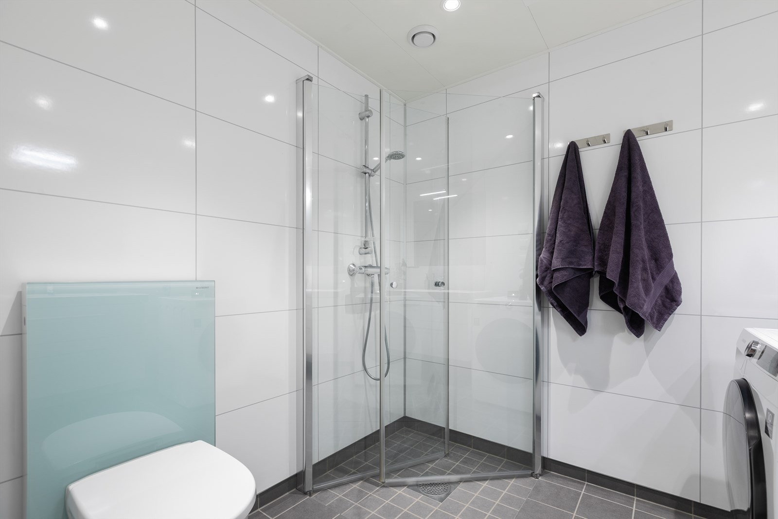 Dusjhjørne med praktiske, innfellbare dører og vegghengt toalett med innebygd sisterne. Galleribilde