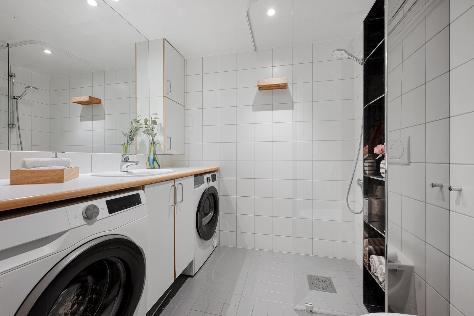 Pent og funksjonelt bad med flislagte vegger og gulv i lyse, tidløse toner. Det er opplegg for vaskemaskin og tørketrommel. Galleribilde