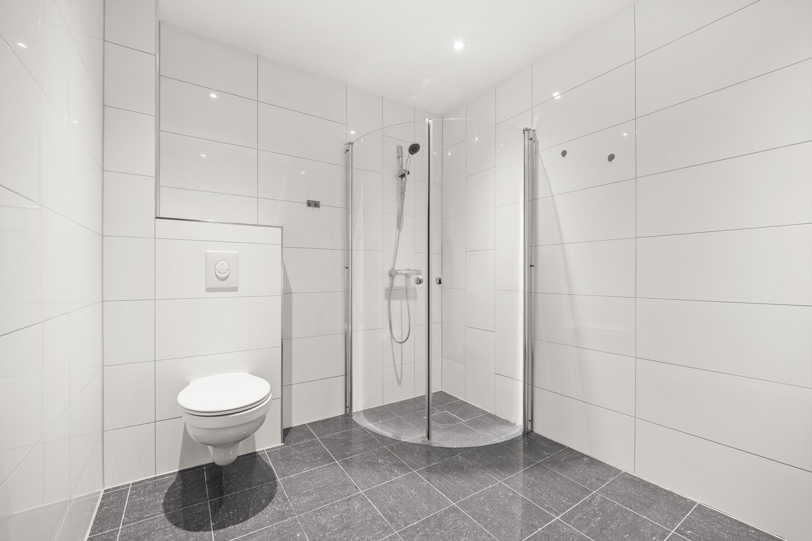 Badet er utstyrt med servant med underskap, speil, veggskap, vegghengt toalett og dusjnisje med innfellbare dører Galleribilde