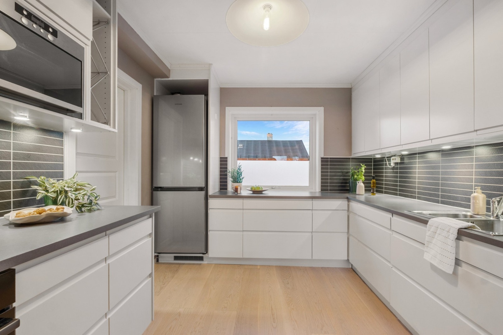 Takhøy innredning med hvite slette fronter og grå benkeplate av laminat. Kitchenboard på vegg over benk. Galleribilde