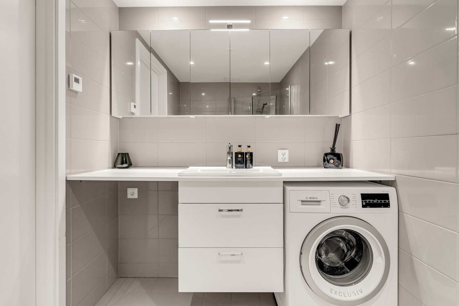 Rommet er innredet med veggmontert wc, servant og blandebatteri i baderomsinnredning, dusjhjørne og opplegg for både vaskemaskin og tørketrommel. Galleribilde