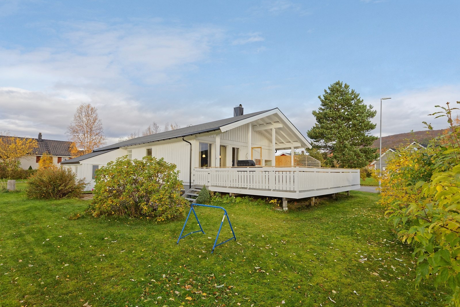 Tomten er opparbeidet med singel på parkeringsområdet, plen, buskvekster, og betongheller på vestre side av huset. Galleribilde