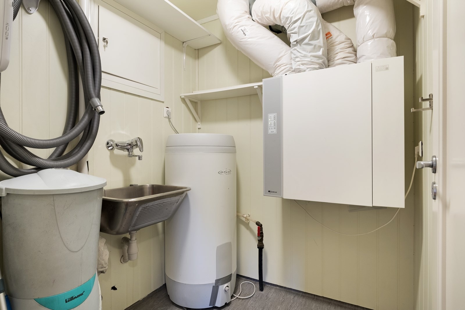 Det tekniske rommet inneheld bl.a. sikringsskåp, sentralstøvsugar, varmtvasstank og utslagsvask i stål. Galleribilde