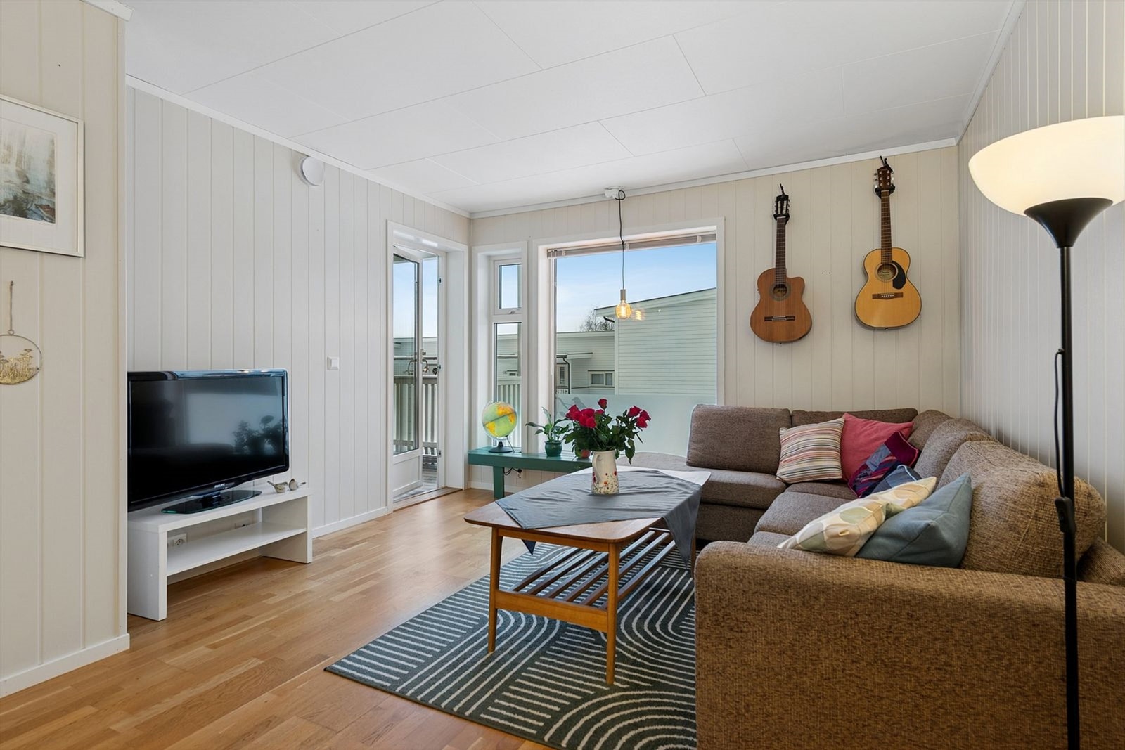 Stuen er et lyst rom med panelplater på veggene og utgang til verandaen. Galleribilde