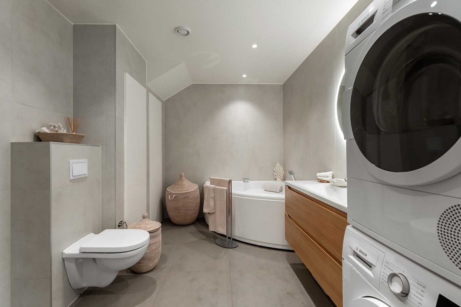 Lekkert flislagt baderom med hjørnebadekar og opplegg for vaskemaskin Galleribilde