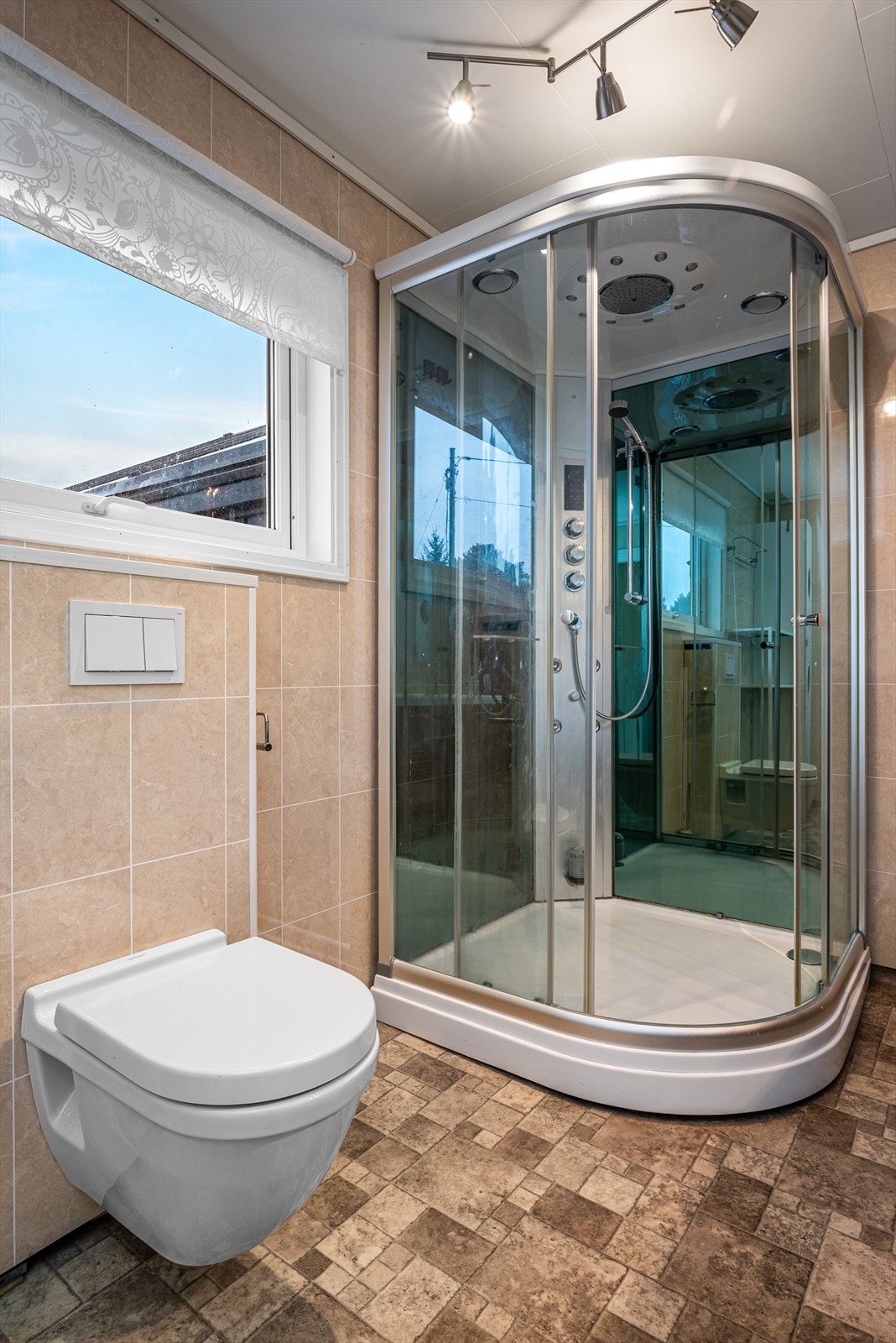 Rommet har behagelig gulvvarme og er innredet med servantskap med dobbel heldekkende servant, speilskap, høyskap, vegghengt toalett, opplegg for vaskemaskin og dusjkabinett. Galleribilde