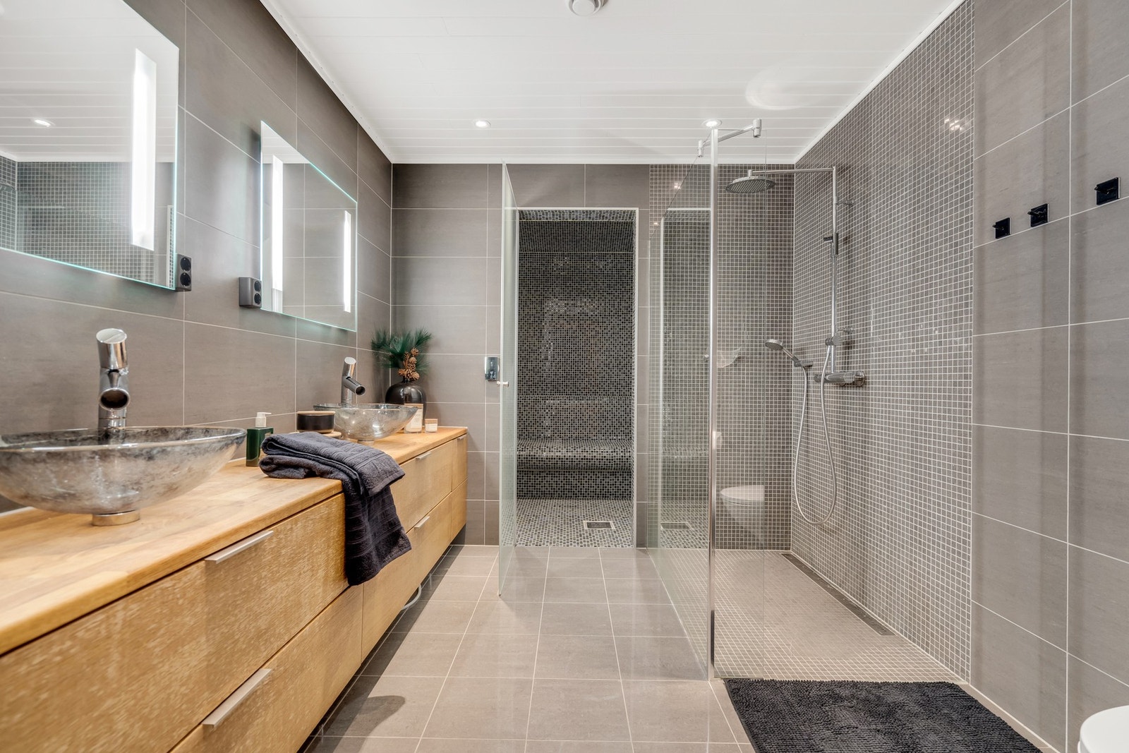 Stort og romslig bad - komplett flislagt med varme i gulvet, heltre innredning, to vasker og to lysspeil. Smakfullt dusjhjørne belagt med mosaikkfliser gir en eksklusiv finish med direkte adkomst inn i et tyrkisk dampbad. Galleribilde