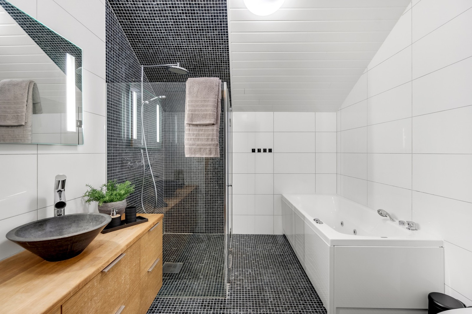 Bad i 2. etasje med heltre innredning, moderne vask og lys speil. Rommet byr på både boblebad og dusjnisje med elegante mosaikkfliser - og selvsagt varme i gulvet for ekstra komfort. Galleribilde