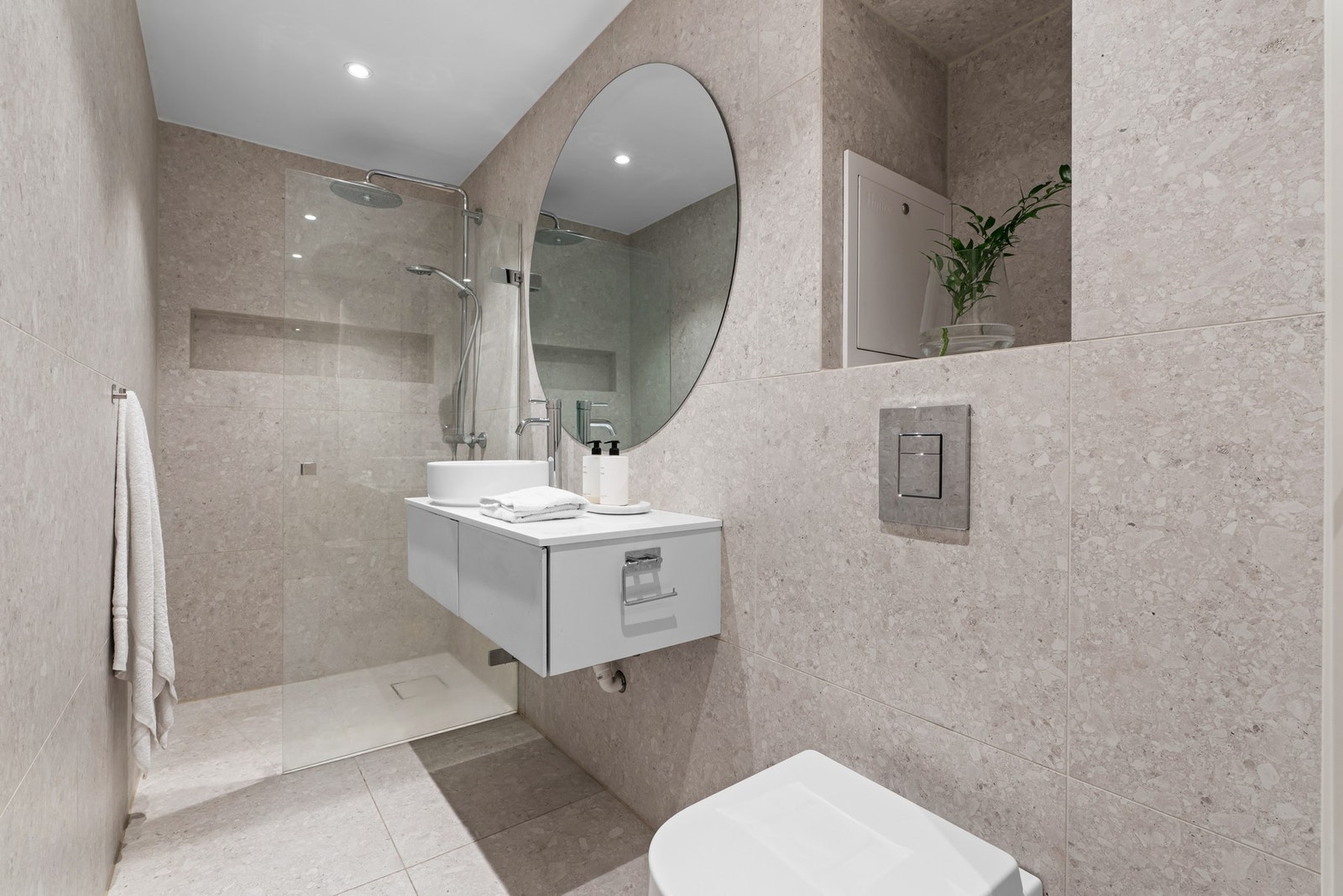 Lekkert bad med store, lyse gulvfliser med varmekabler, matchende veggfliser og downlights i himling. Galleribilde