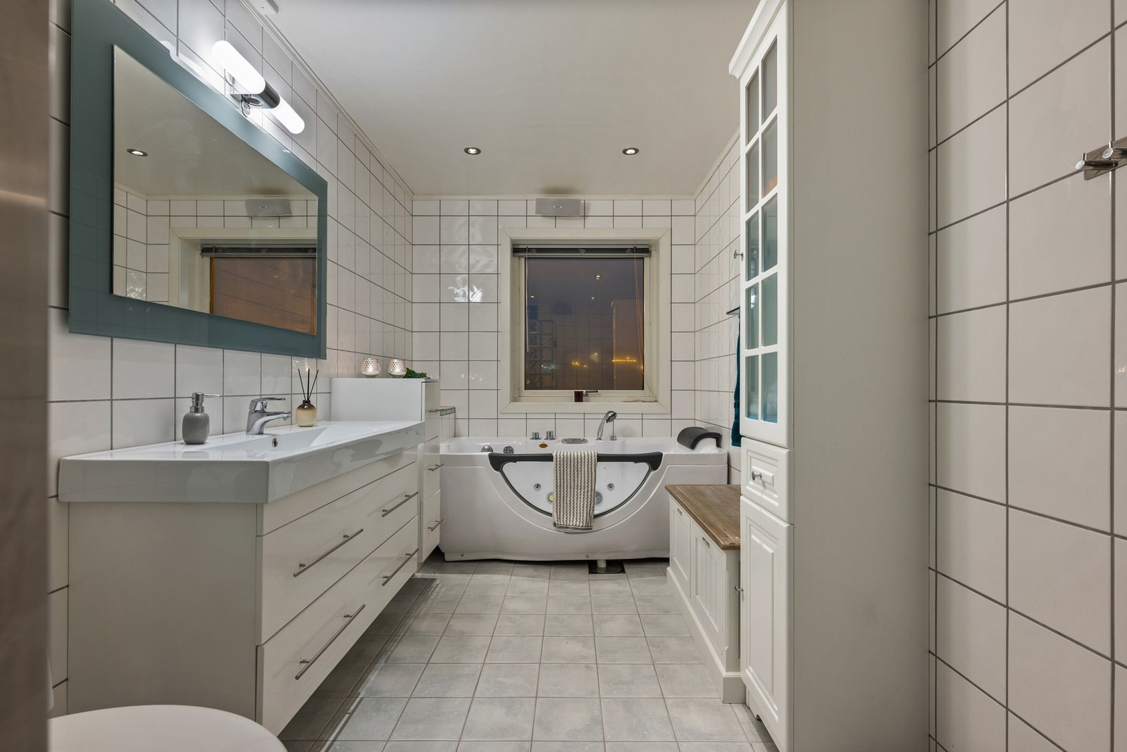 Et tidløst baderom med flislagte overflater, heldekkende servant, speil, badekar, toalett og dusjhjørne. Galleribilde