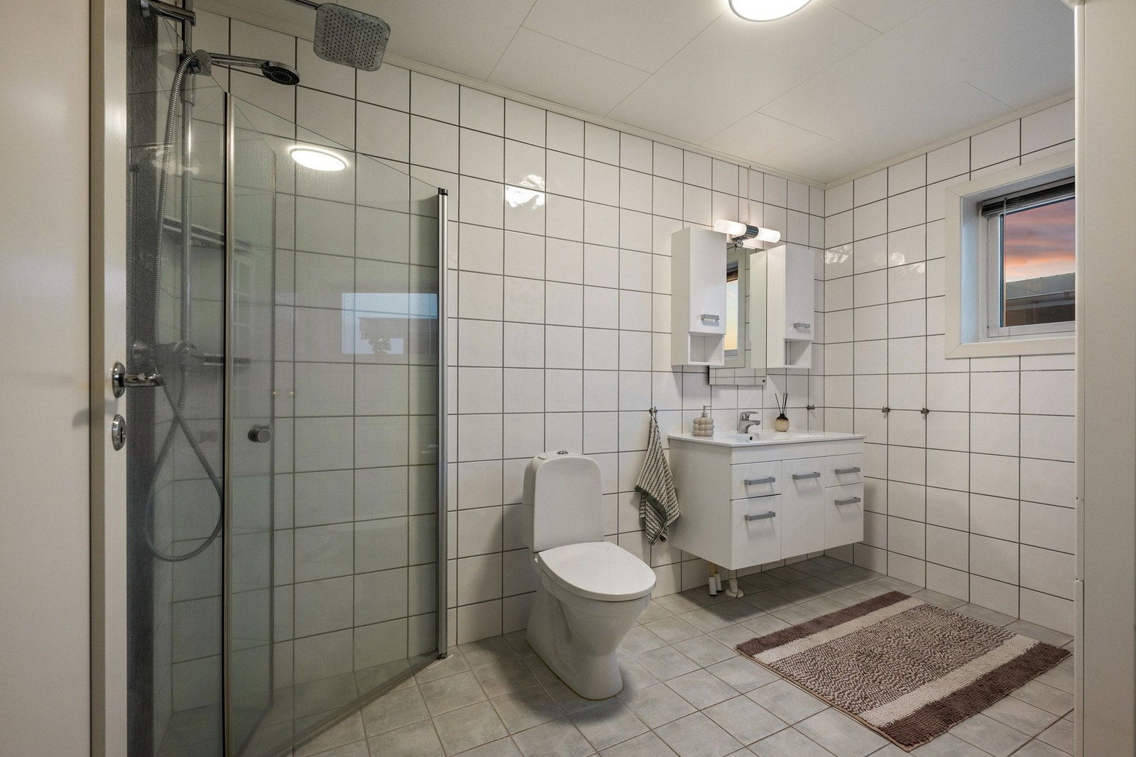 Baderommet i boligens 1. etasje med flislagt gulv og utstyrt med dusj, servant og toalett. Galleribilde