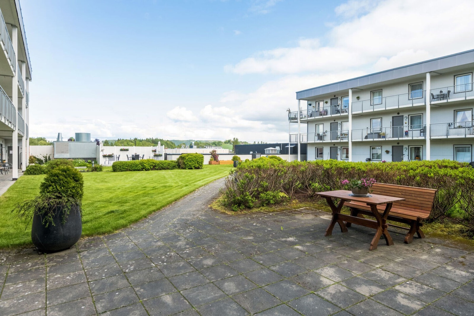 Pent opparbeidet uteområde med benker, prydbusker og bed. Galleribilde