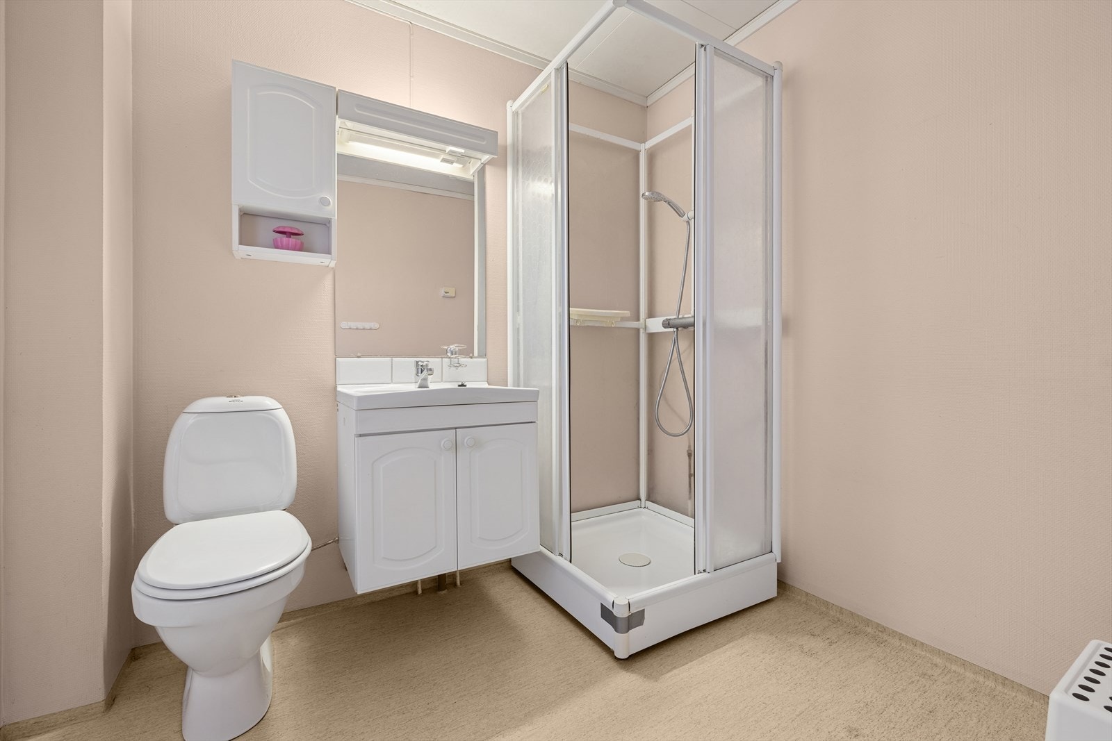 Badet har en enkel og praktisk utforming med linoleum gulv, dusjkabinett, servantseksjon med skap, gulvmontert toalett og opplegg for vaskemaskin. Galleribilde