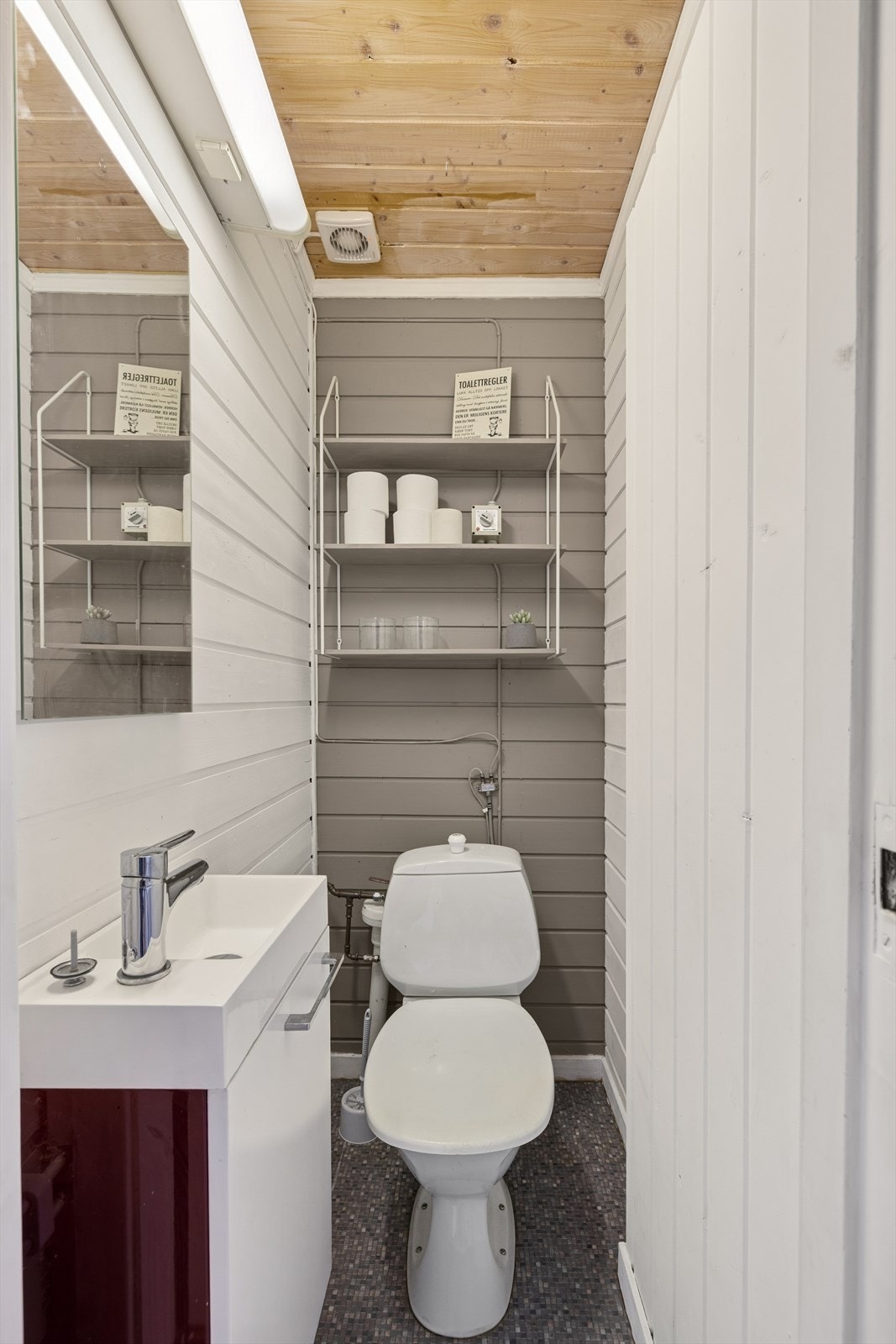 WC-rommet er funksjonelt innredet med toalett, servant med underskap og speil, og tilbyr praktiske løsninger i en kompakt og stilren utforming. Galleribilde