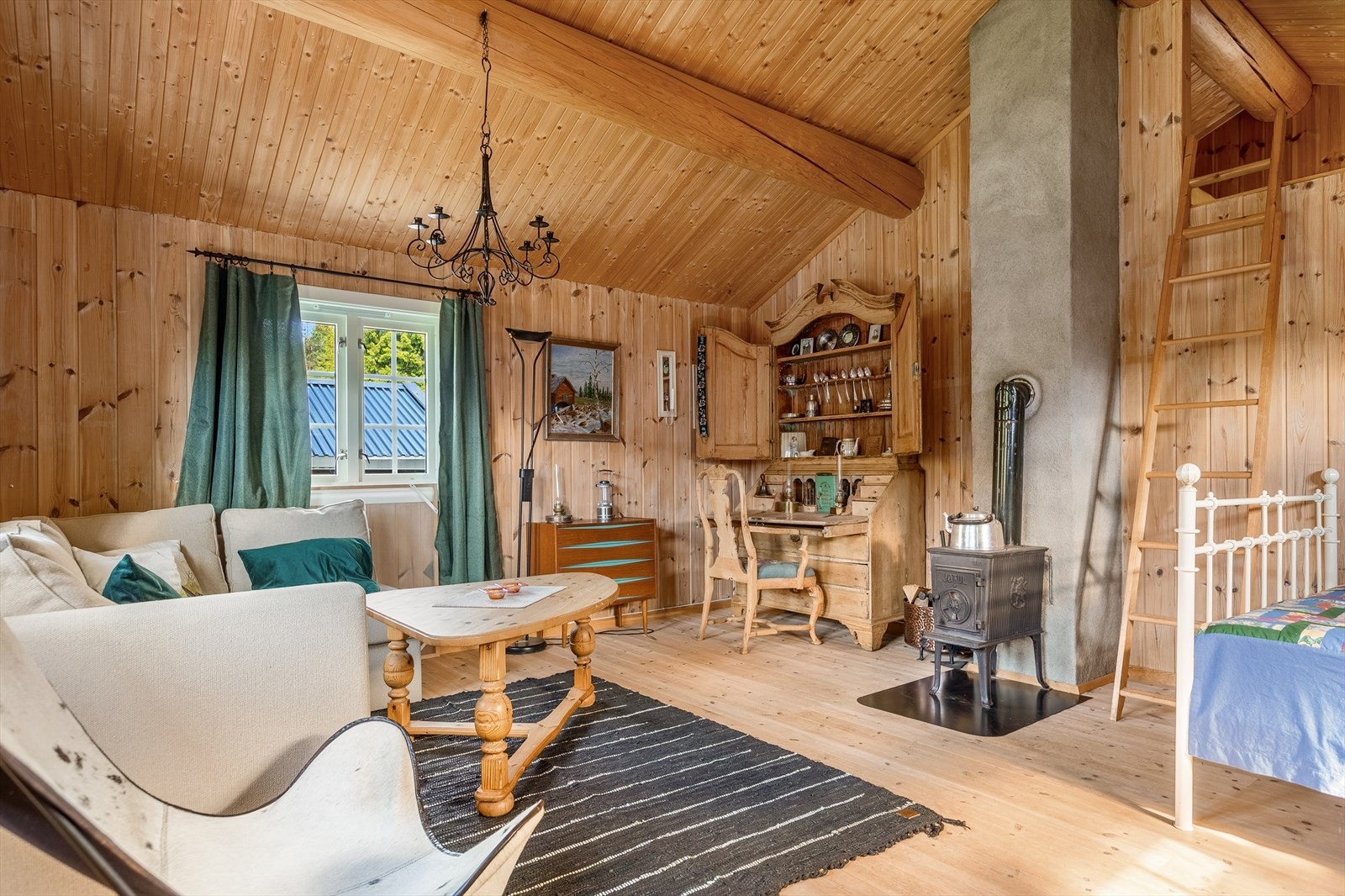 Lys og åpen stue med behandlet panel på veggene, mønet himling med tre tømmeråser og stige opp til liten hems. Galleribilde