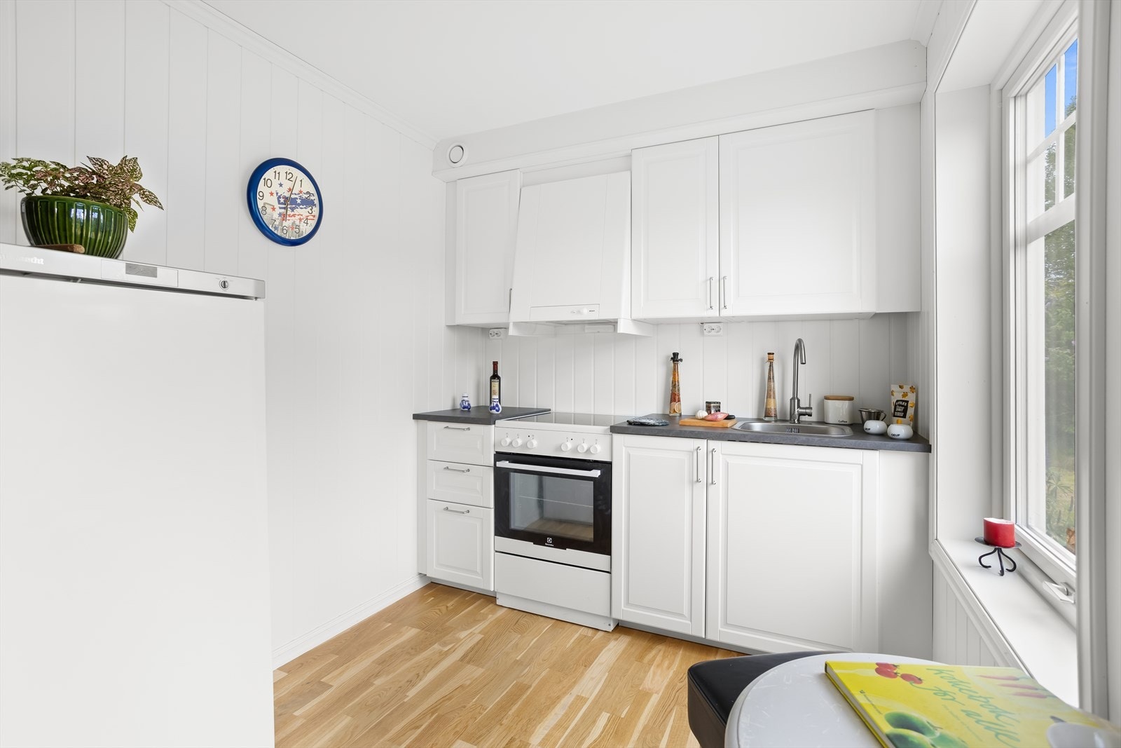 Hvit kjøkkeninnredning med profilerte fronter, laminat benkeplate og og overskap som når opp til tak. Galleribilde