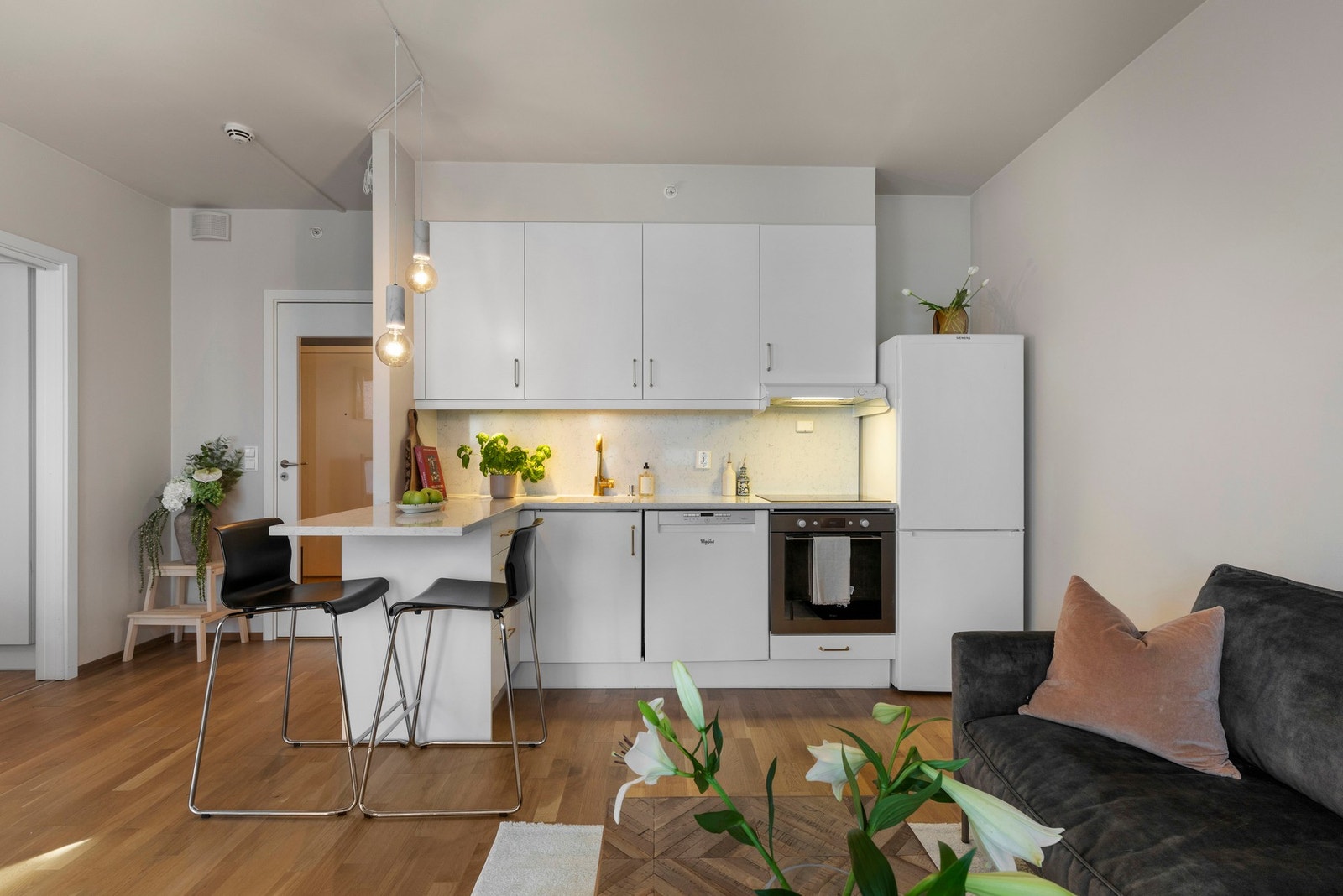 Kjøkkenet har en innholdsrik kjøkkeninnredning med foring mot tak, hvite glatte fronter og en lys steinbenkeplate av Quarts Galleribilde