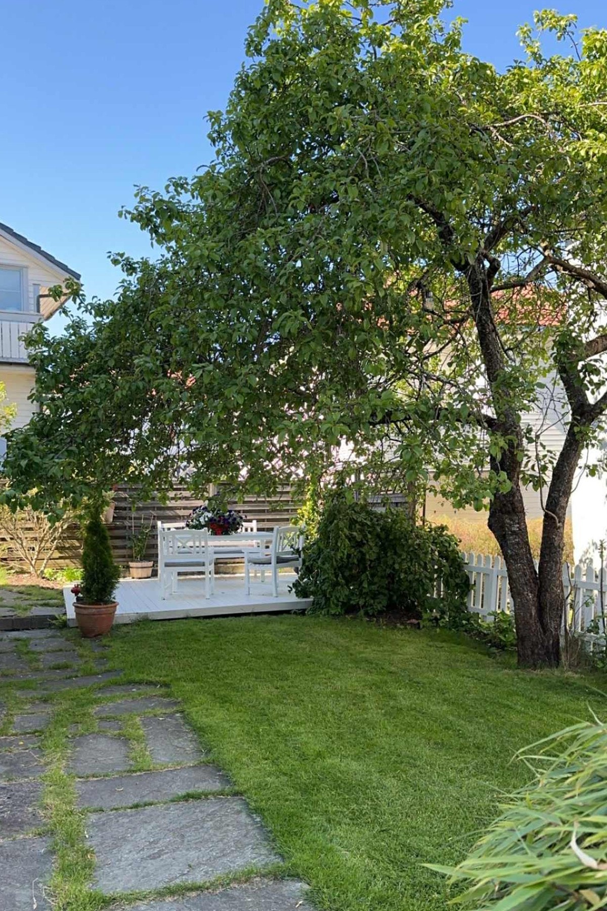 Uteområdet har plen og en terrasse med sitteplass under et stort tre. Galleribilde