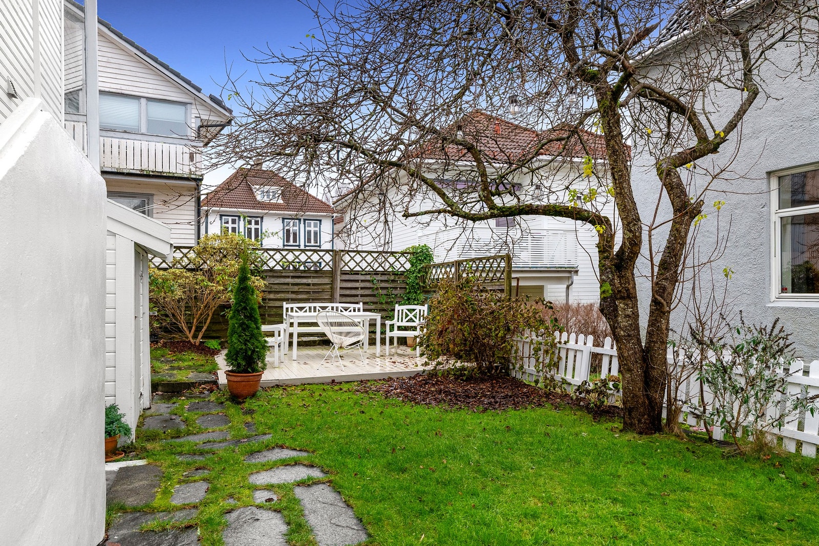 Hage med plen, steinlagt gangsti og terrasse. Omgitt av hus og gjerde. Galleribilde
