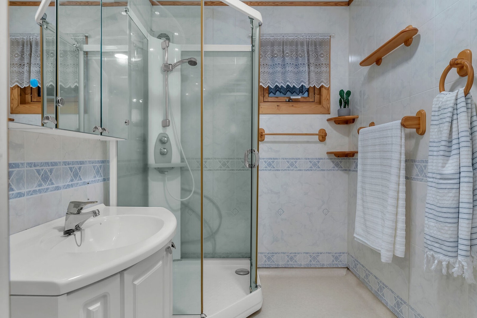 Eldre bad med baderomsplater på veggene og vinylbelegg på gulv. Rommet har innredning med servant, speilskap og dusjkabinett. Galleribilde