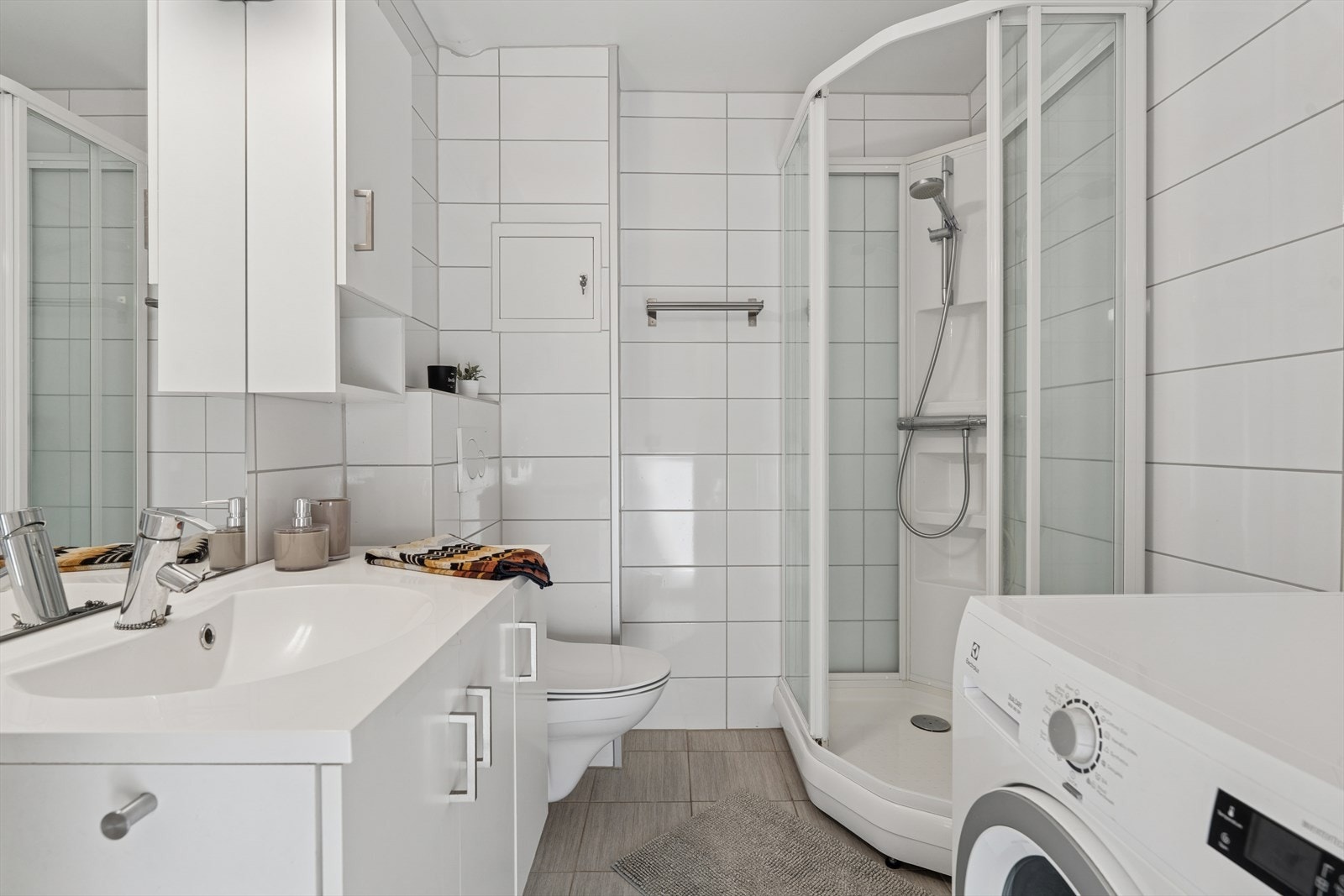 Bad med vegg hengt toalett, servant med underskap, opplegg til vaskemaskin og dusjkabinett. Galleribilde