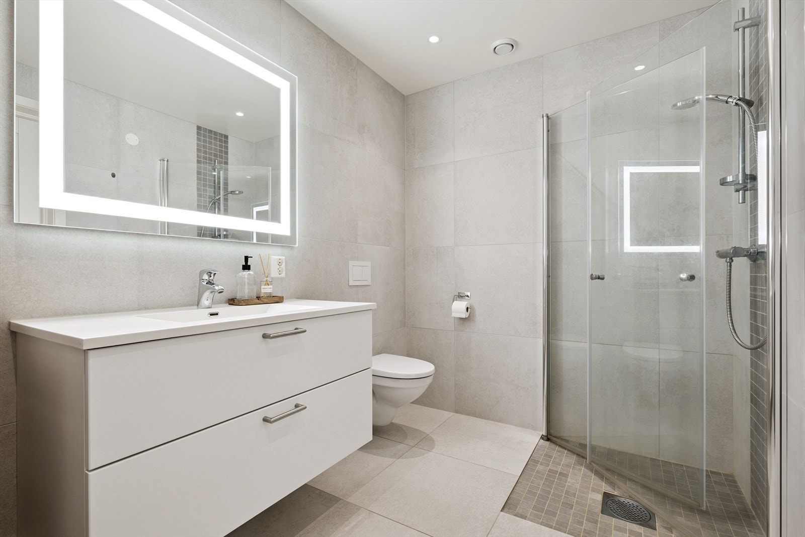 Flislagt delikat bad med servant skap med skuffer, toalett og dusjhjørne. Galleribilde