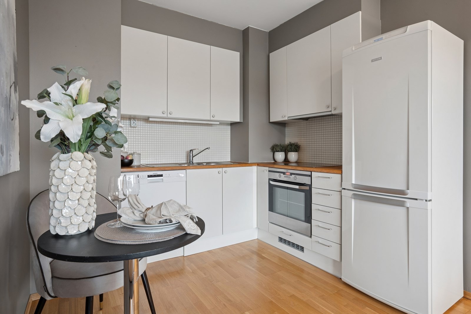 Fint lyst kjøkken med malte, glatte fronter og heltre benkeplate. Mosaikkfliser mellom benk og overskap skaper et fint uttrykk. Galleribilde