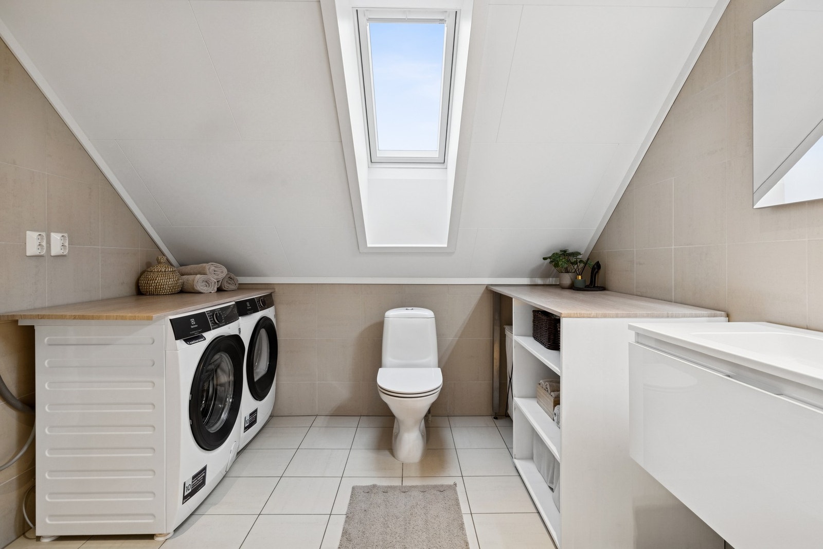 Baderom med fliser på gulv og vegger, hvit servantinnredning med skuffeseksjon, dusjhjørne med glassdører, opplegg for vaskemaskin og gulvstående toalett. Galleribilde