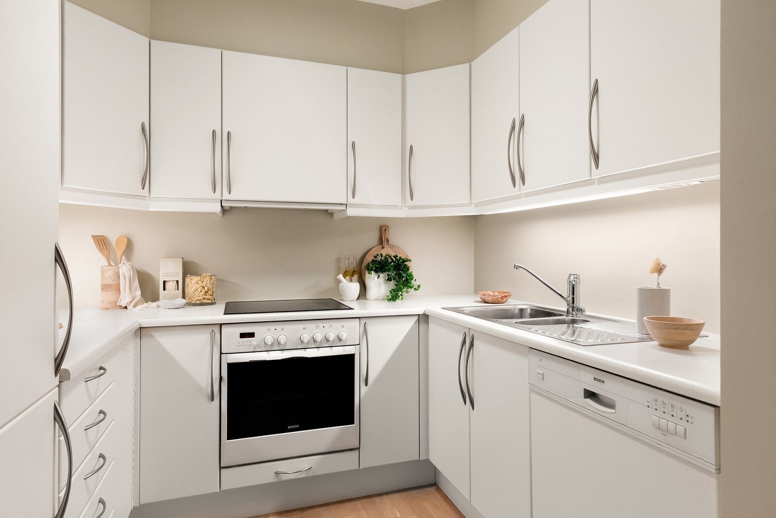 Kjøkkeninnredningen er utstyrt med hvite, glatte fronter og benkeplate i laminat med nedfelt kum i rustfritt stål. Innredningen er utstyrt med helintegrerte hvitevarer som platetopp, stekeovn, oppvaskmaskin og kjøle-/fryseskap. Galleribilde