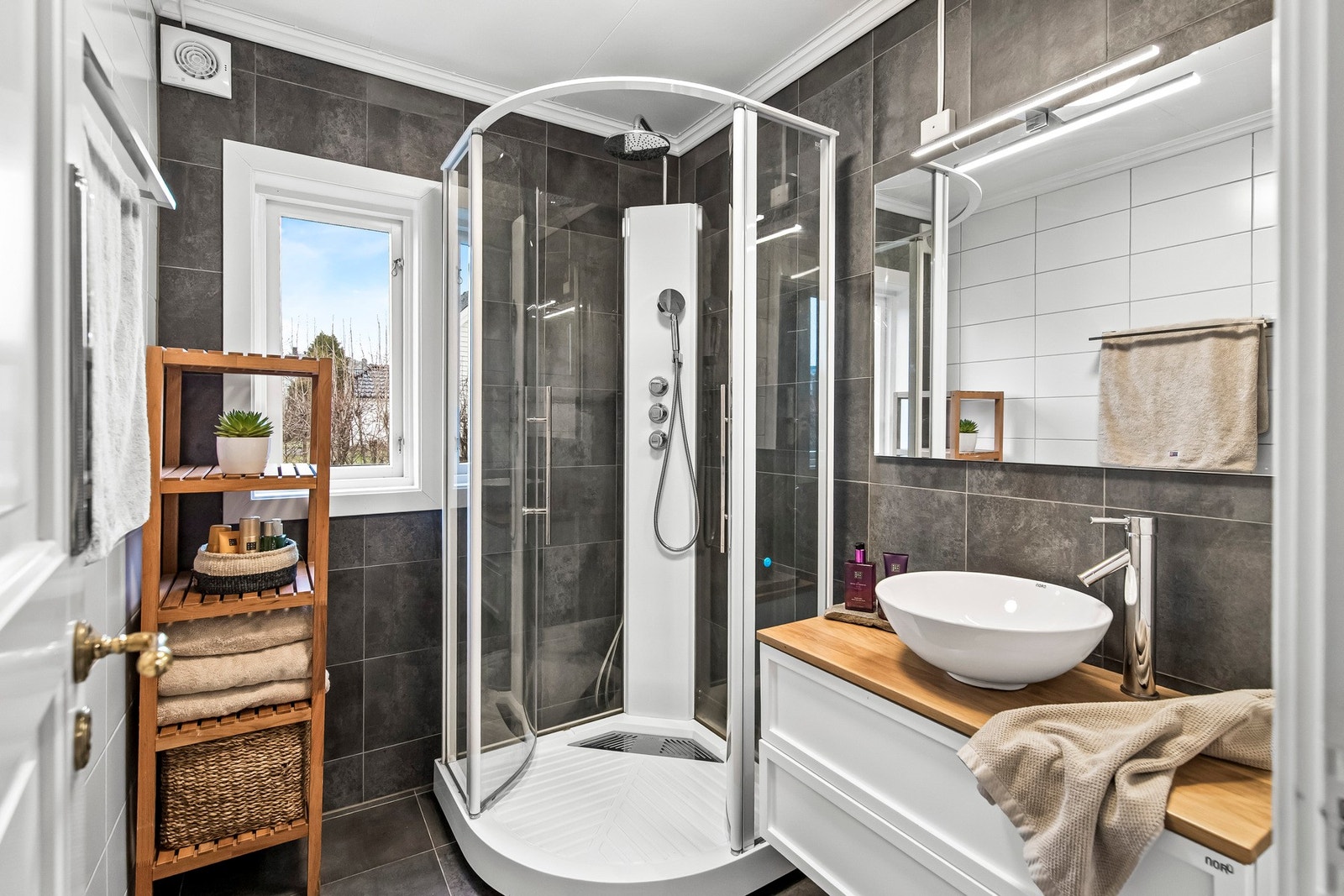 Baderomsinnredningen består av et speil med belysning og en hvit skuffeseksjon med toppmontert servantskål. Galleribilde