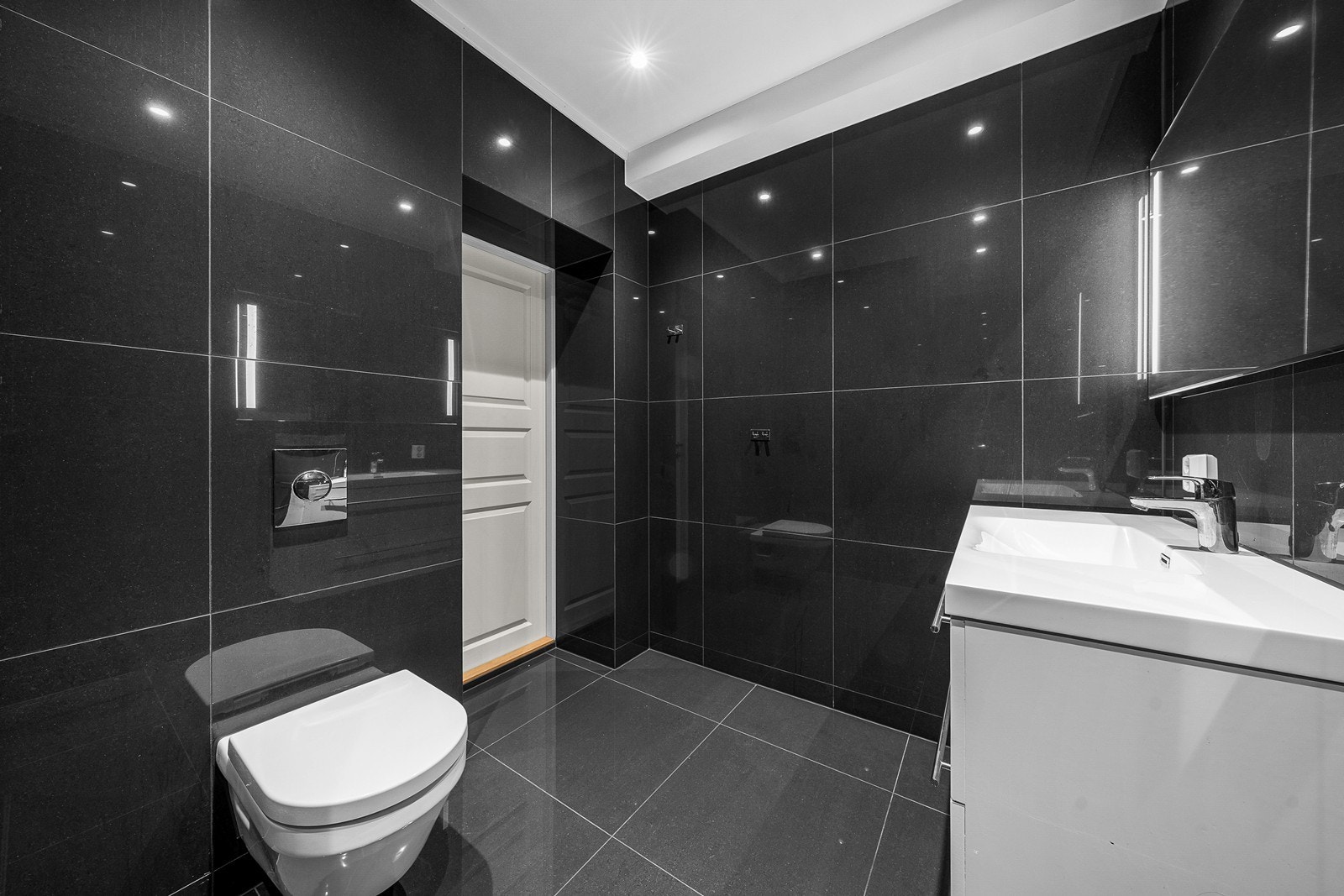 Badet er innredet med vegghengt toalett, servant med skuffeseksjon, speil og dushjørne Galleribilde