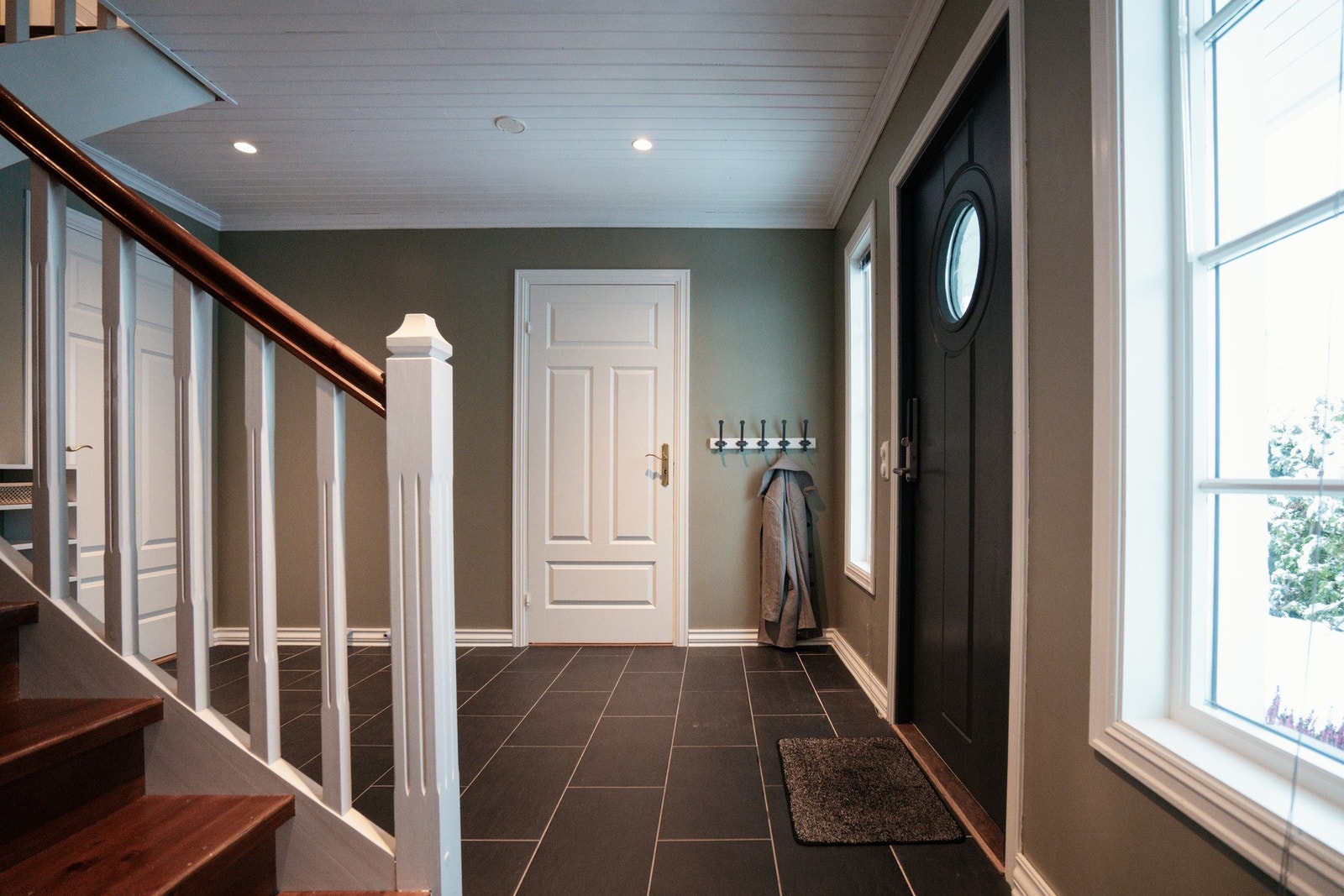 Romslig entré/hall med flislagt gulv, slette vegger og panel i himling med downlights Galleribilde