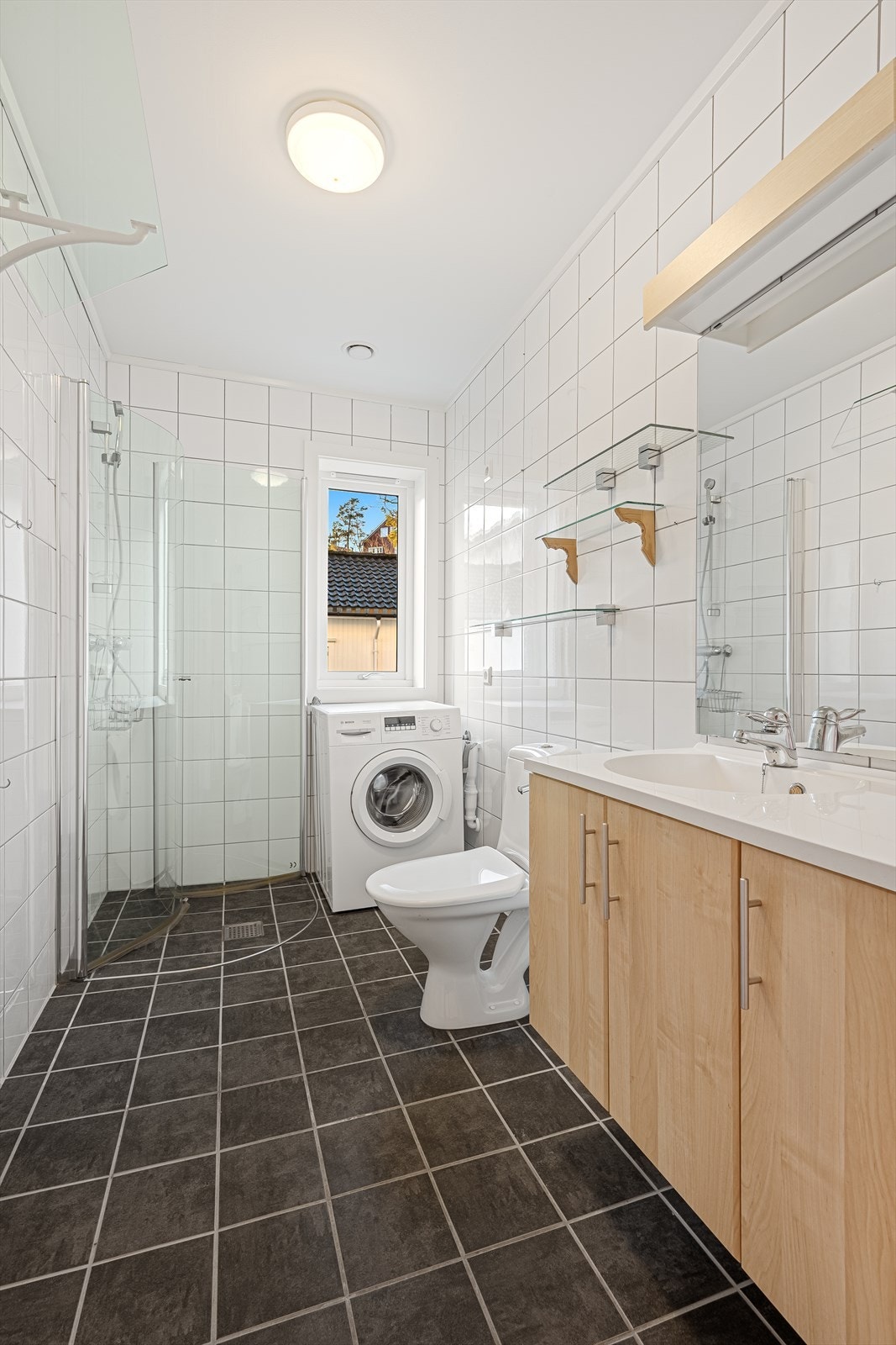 Badet er flislagt og inneholder dusjhjørne, toalett, opplegg til vaskemaskin og servant med underskap. Vaskemaskin medfølger. Galleribilde