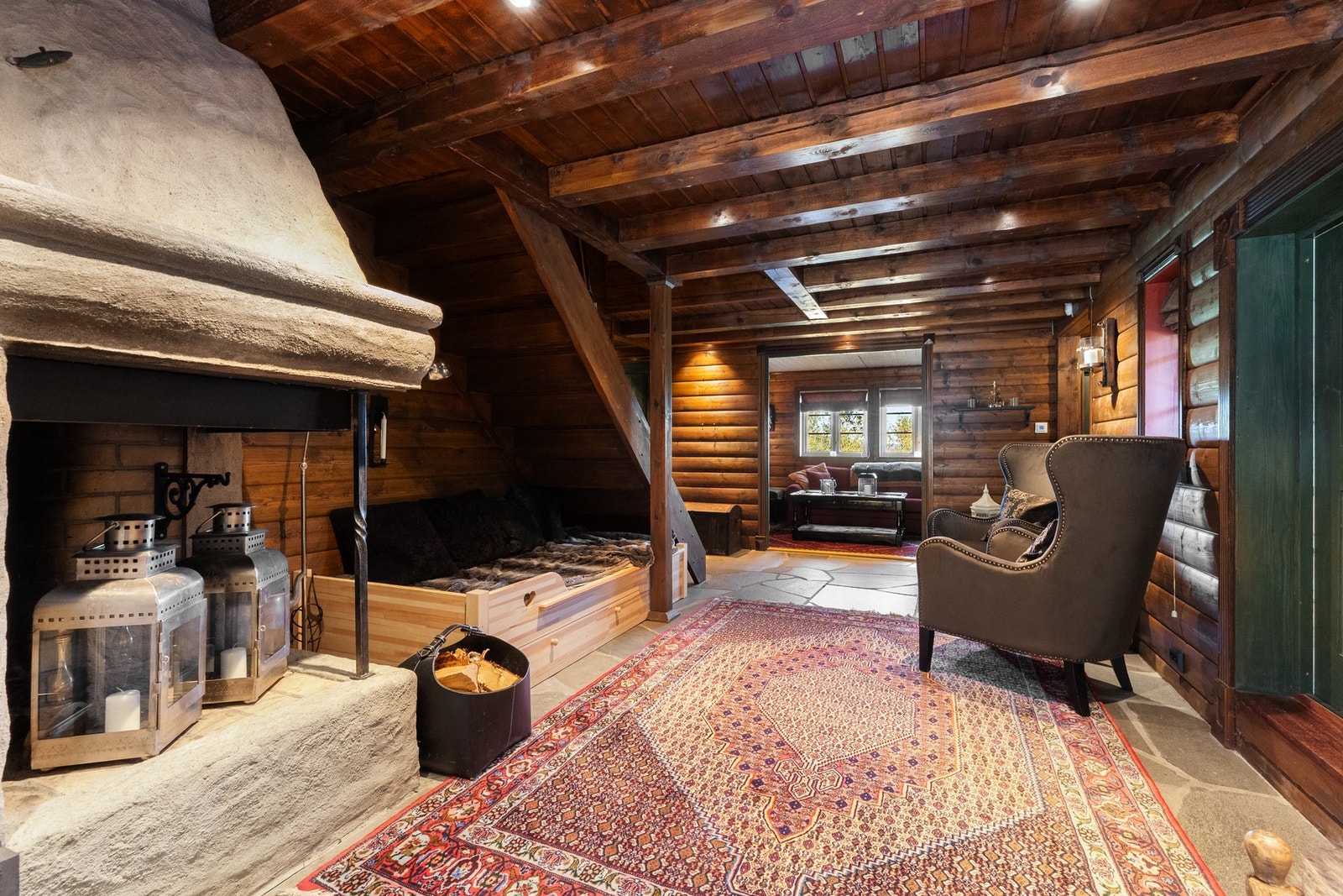 Innbydende hall med skiferfliser og en stemningsfull gruepeis. Dette er en sone som umiddelbart setter tonen for resten av hytta - lunt og med ekte fjellhyttestemning. Her er det lett å se for seg en kopp kaffe og en god bok foran peisen, mens hundene hvi Galleribilde