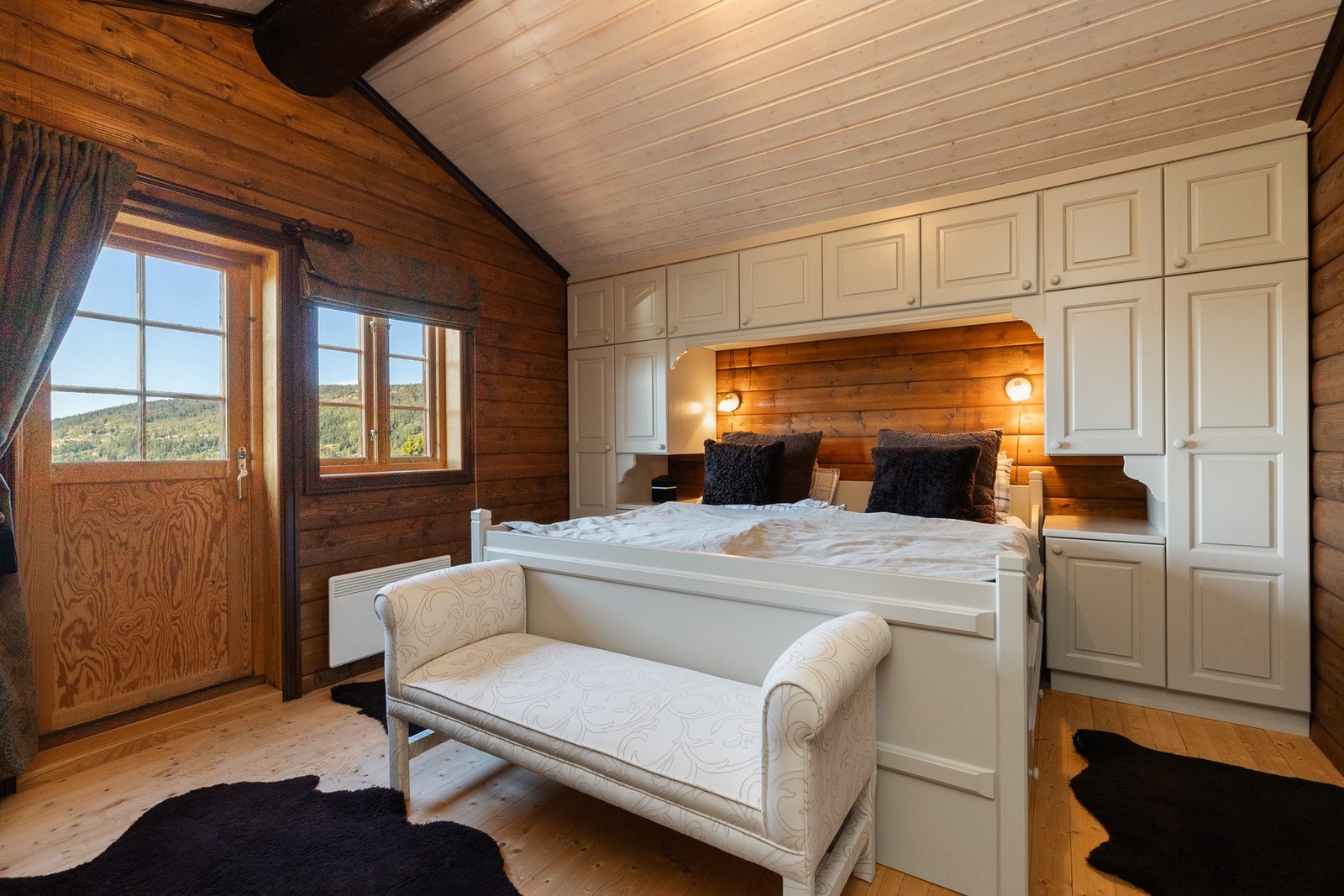 Romslig soverom med dobbeltseng som har skuffer i sokkel, plassert mellom stedbygde skap Galleribilde